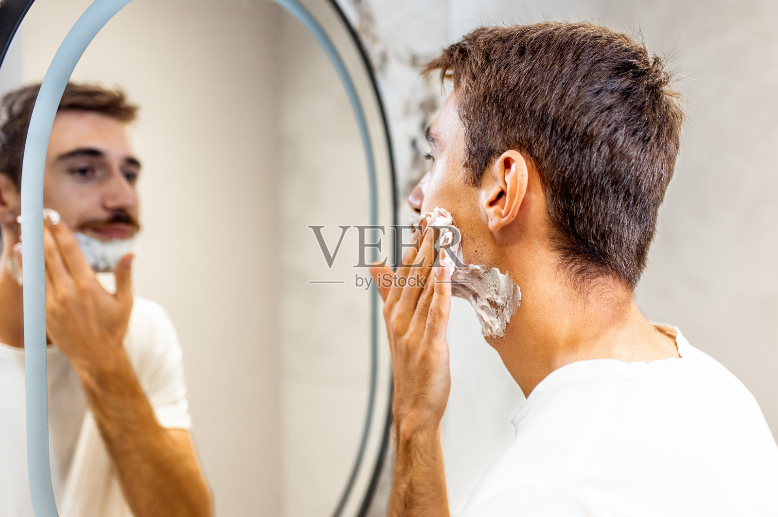 一个留着胡子的男人在浴室镜子前涂抹剃须泡沫。照片摄影图片
