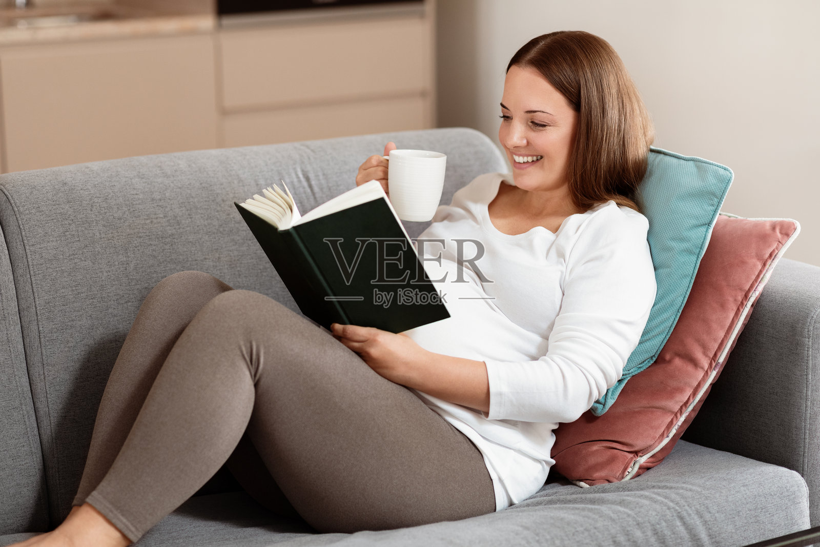 女人在沙发上放松,享受着一本书和一杯茶照片摄影图片