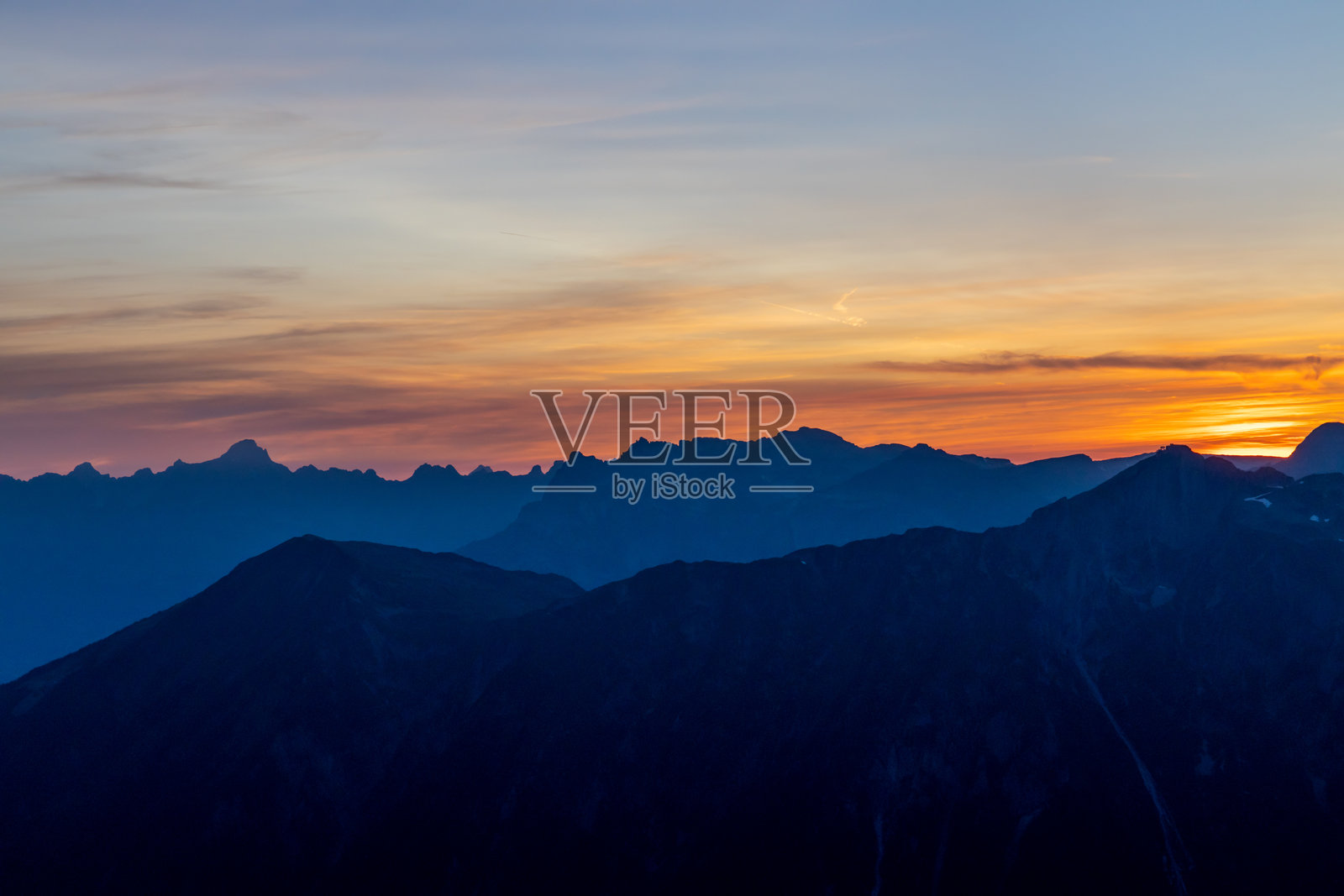 日落时分,红色和橙色的天空在阿尔卑斯山的雪峰和岩石山脉上空燃烧。照片摄影图片