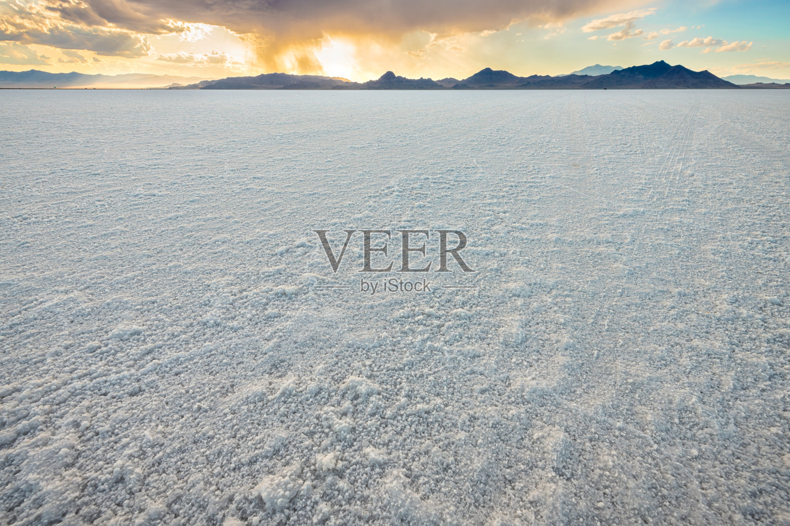 博内维尔盐滩的低角度视图,蓝色和黄色的多彩日落景观,位于犹他州盐湖城,背景有山脉和戏剧性的阳光与云彩。照片摄影图片