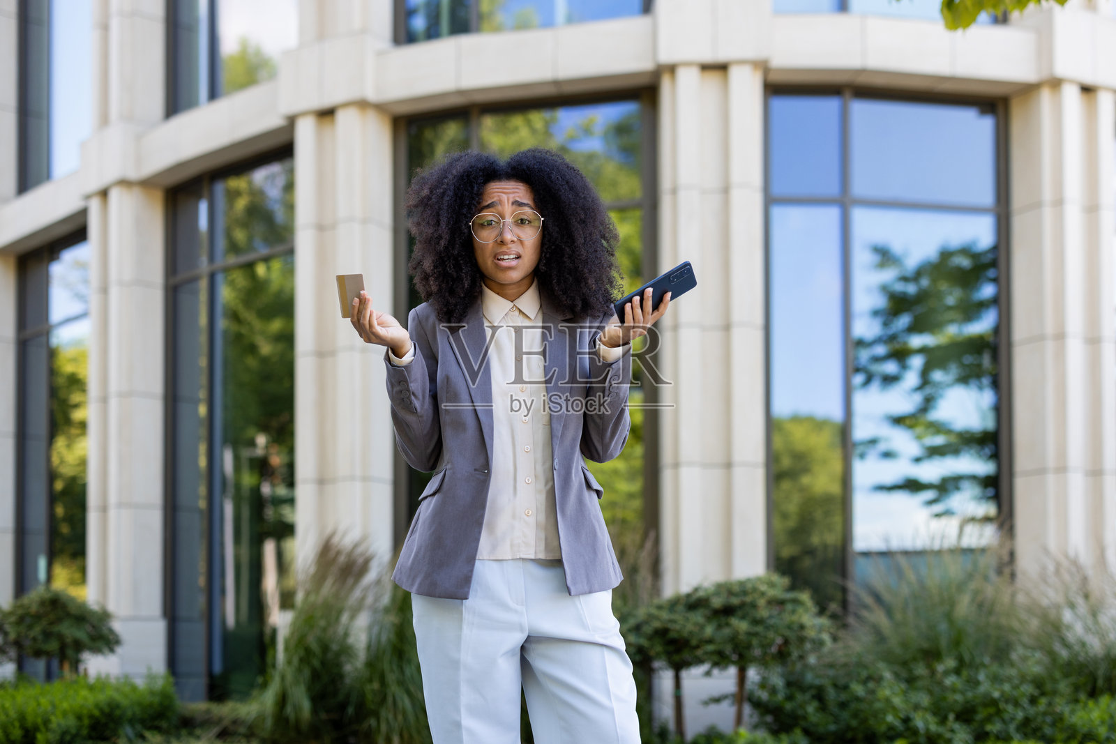 非裔美国女商人在办公大楼外面,手持智能手机和信用卡,面露对现代科技的困惑。照片摄影图片