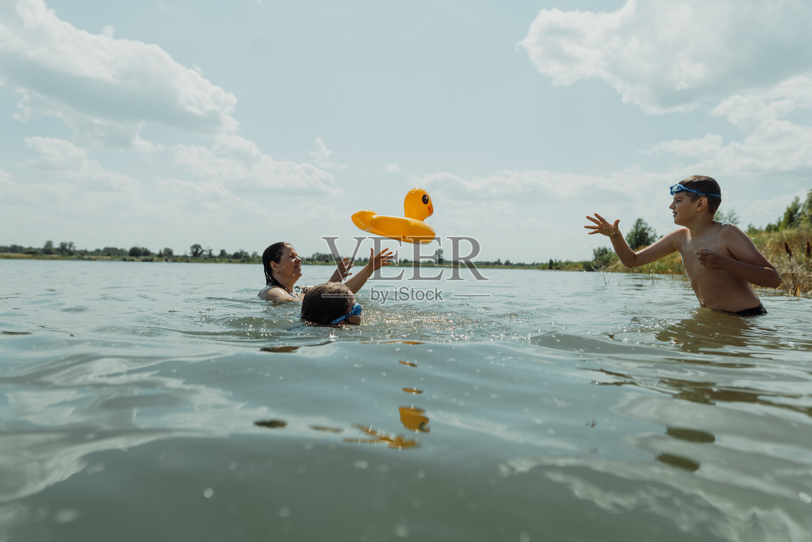家庭在阳光明媚的日子里在湖中玩充气鸭子浮筒照片摄影图片