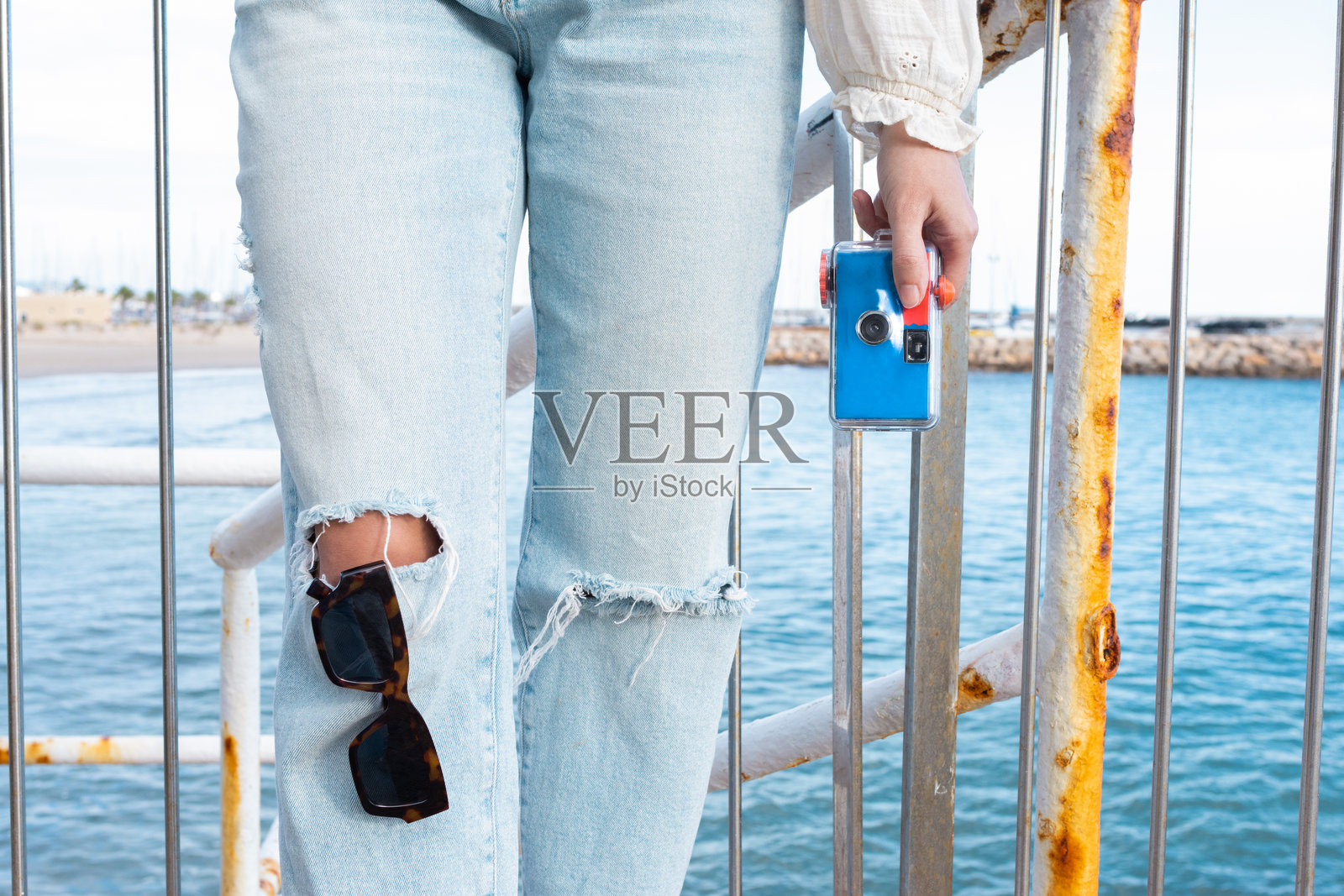 时尚牛仔裤的女性游客在海滨旅游目的地旅行,手中拿着一台紧凑型一次性防水相机,享受旅途中的自由。模拟相机。照片摄影图片