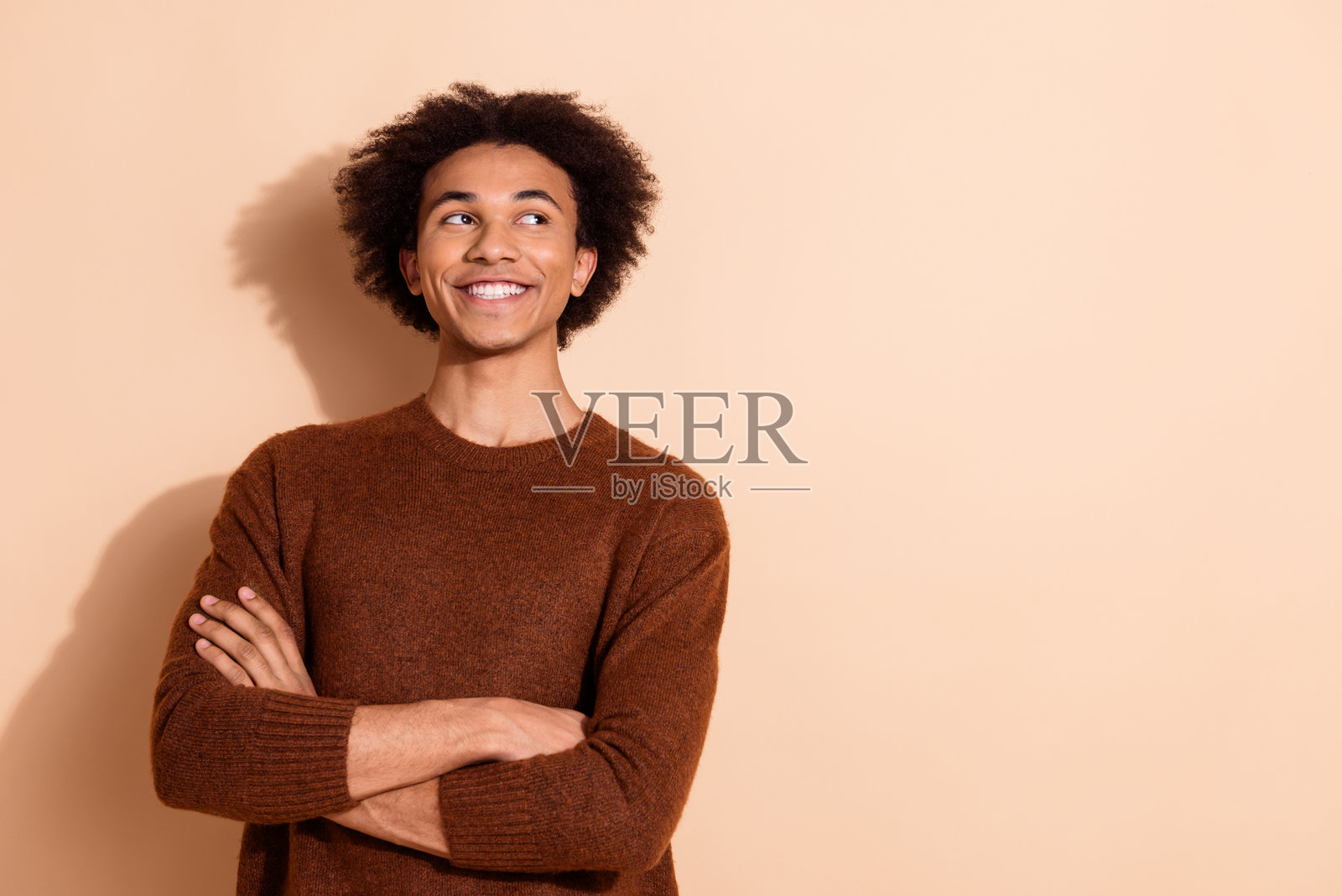 自信的年轻男子穿着休闲服装,微笑着站在米色背景前,适合用于广告或宣传内容。照片摄影图片