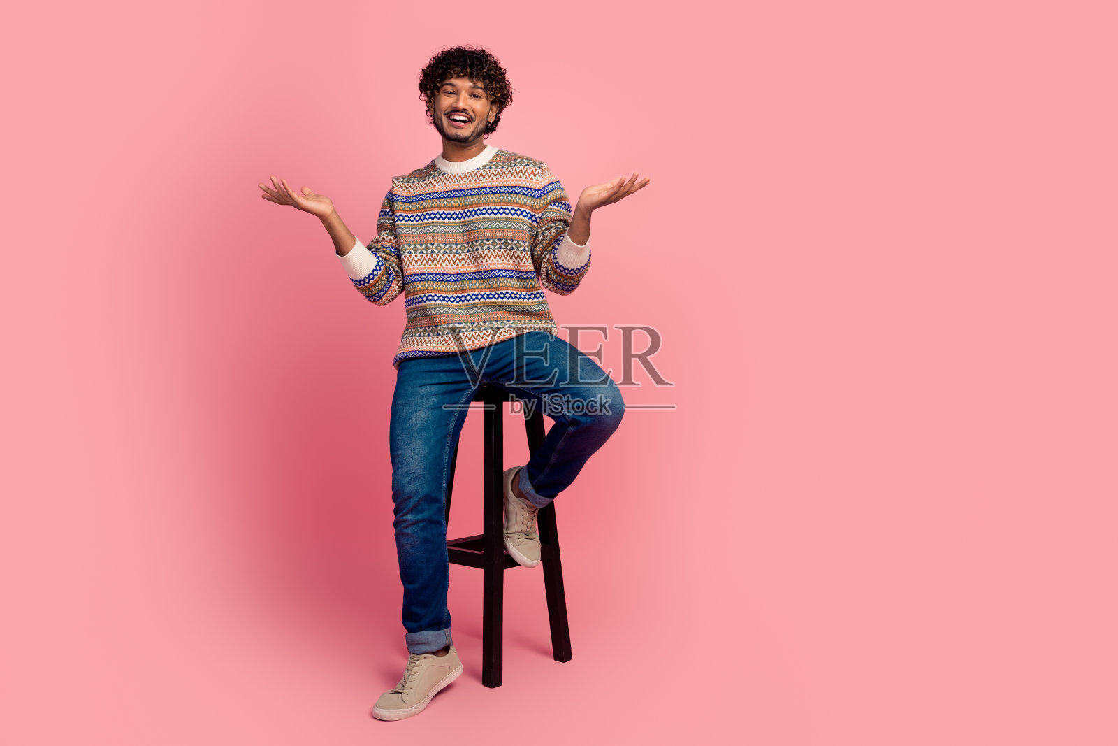 年轻男子坐在凳子上,背景为粉色,周围空旷。照片摄影图片