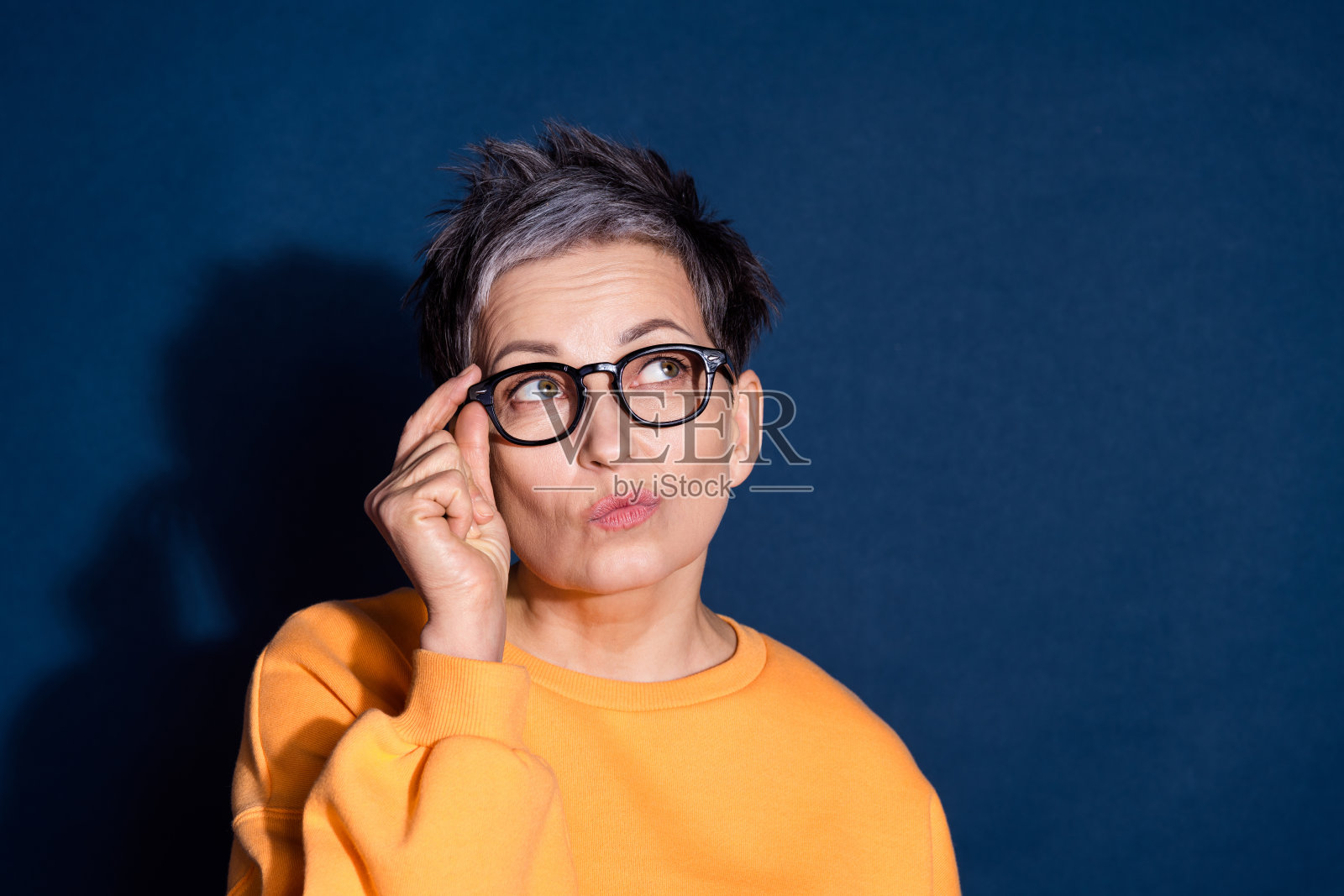 可爱的退休女士的照片肖像,神情怀疑,穿着时尚的黄色服装,背景为深蓝色。照片摄影图片