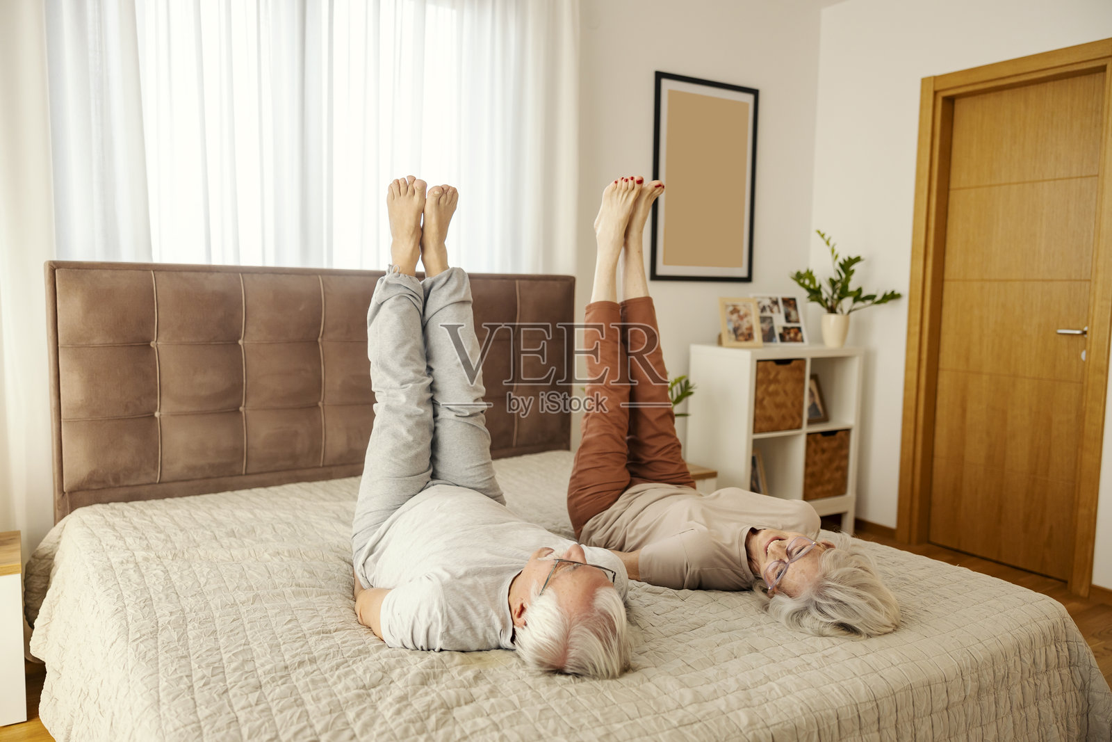 活跃的老年夫妇在舒适的公寓床上做早晨锻炼。照片摄影图片