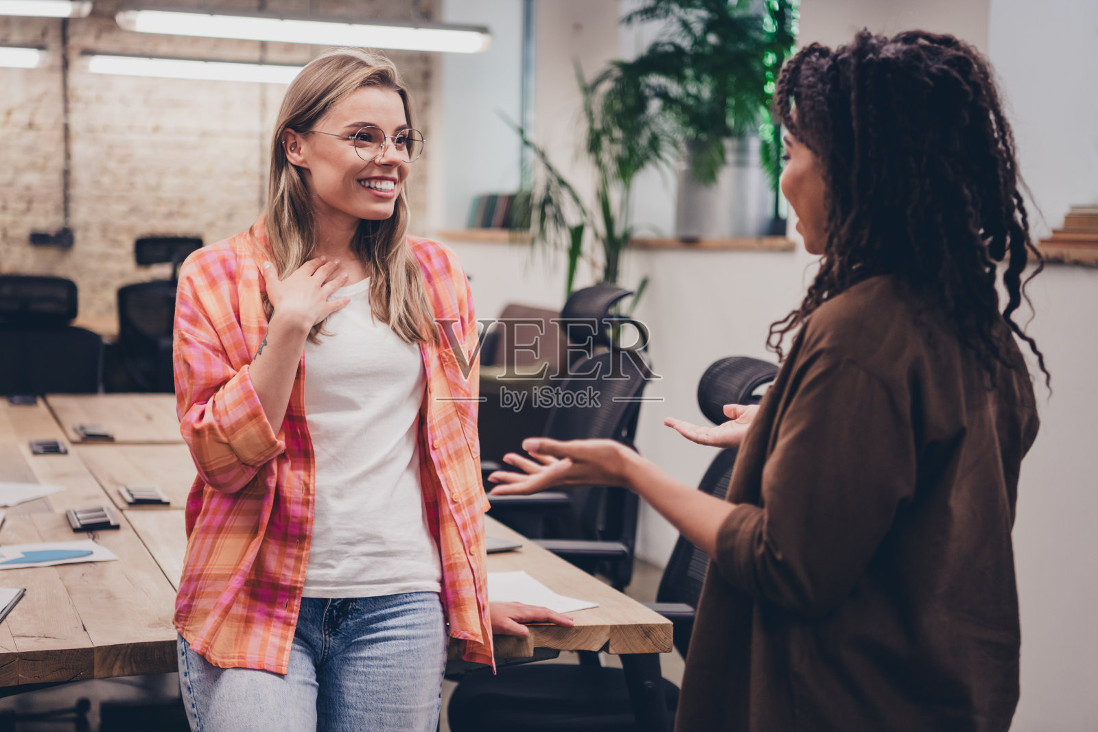 两位企业女员工在室内商务中心微笑交谈,展现合作精神。照片摄影图片