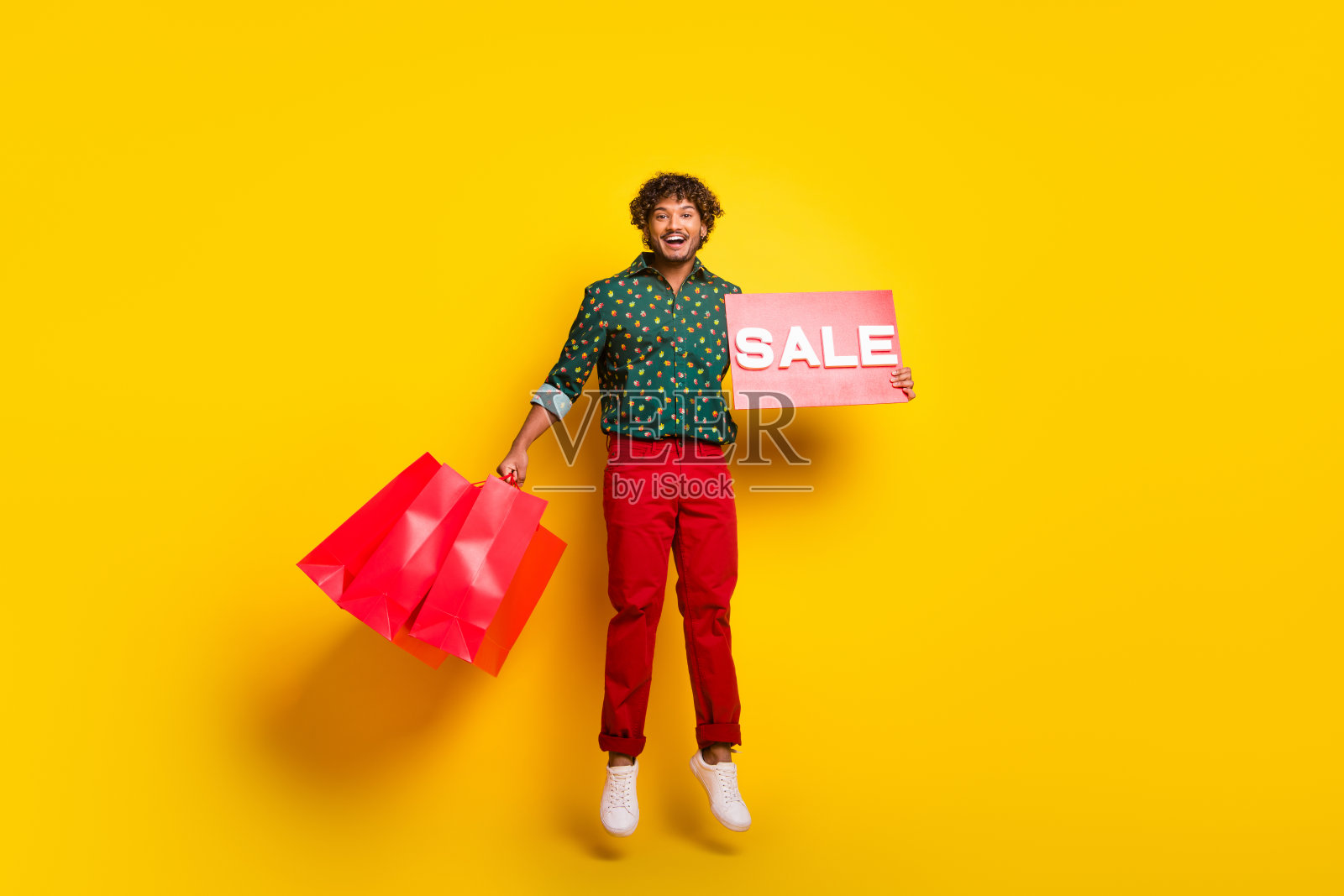 全身肖像,优雅的年轻男士在黄色背景下跳跃,手中拿着空购物袋,穿着衬衫。照片摄影图片