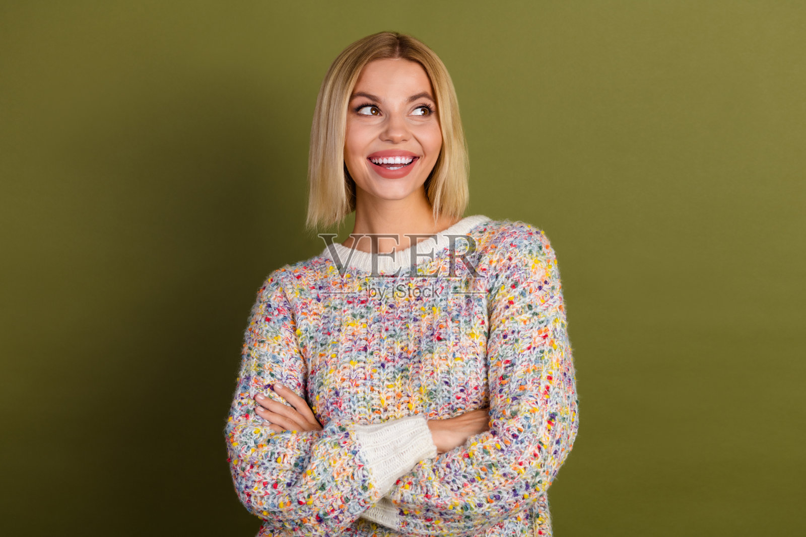 自信的年轻女性,金色头发,穿着色彩斑斓的针织毛衣,背景为卡其色,展现积极的能量和风格。照片摄影图片