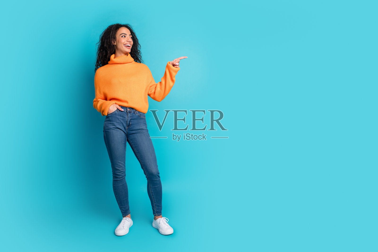 全身肖像,漂亮的年轻女孩指着空白空间,背景为青绿色。照片摄影图片