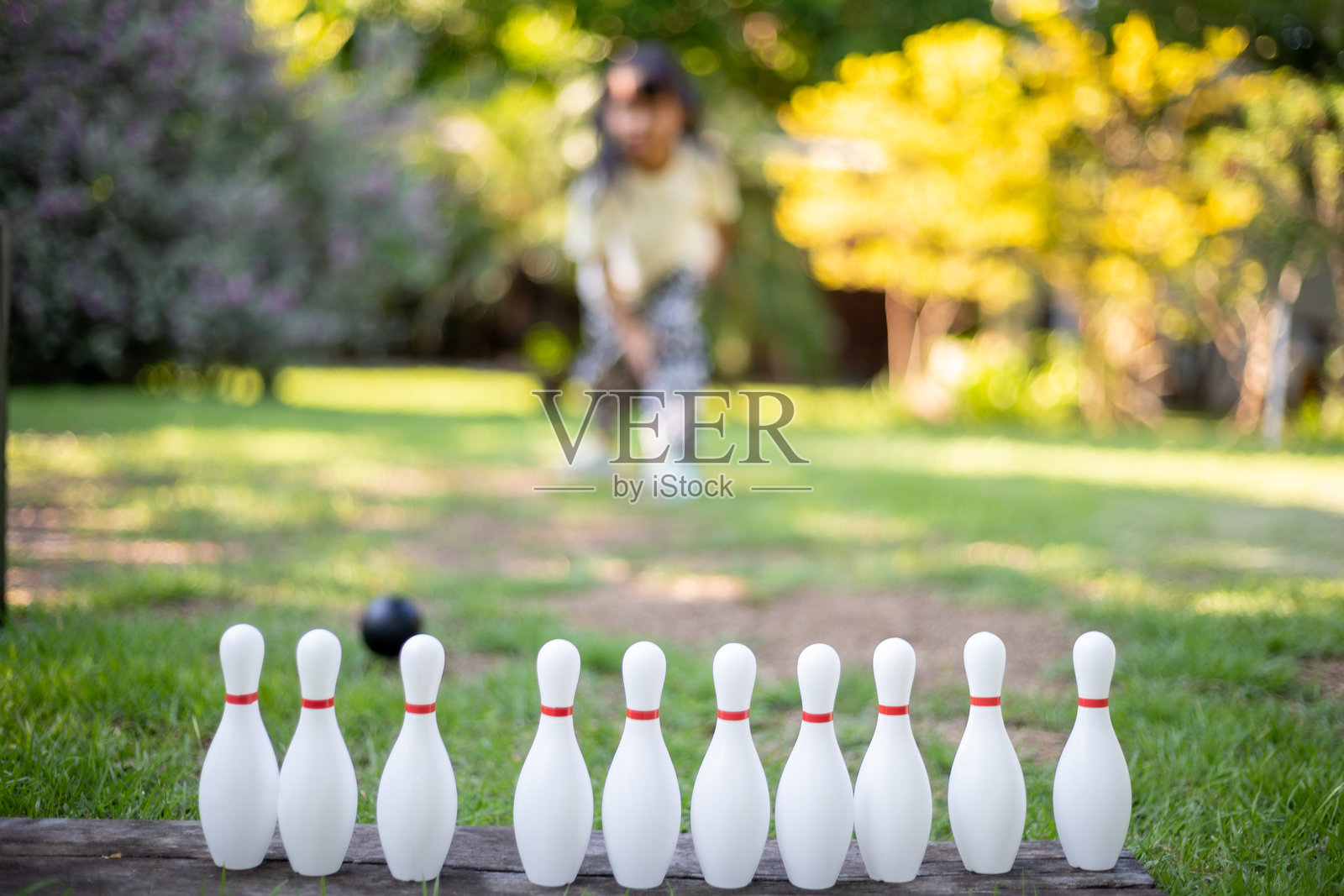 一个小女孩坐在草地上玩一套保龄球瓶。照片摄影图片