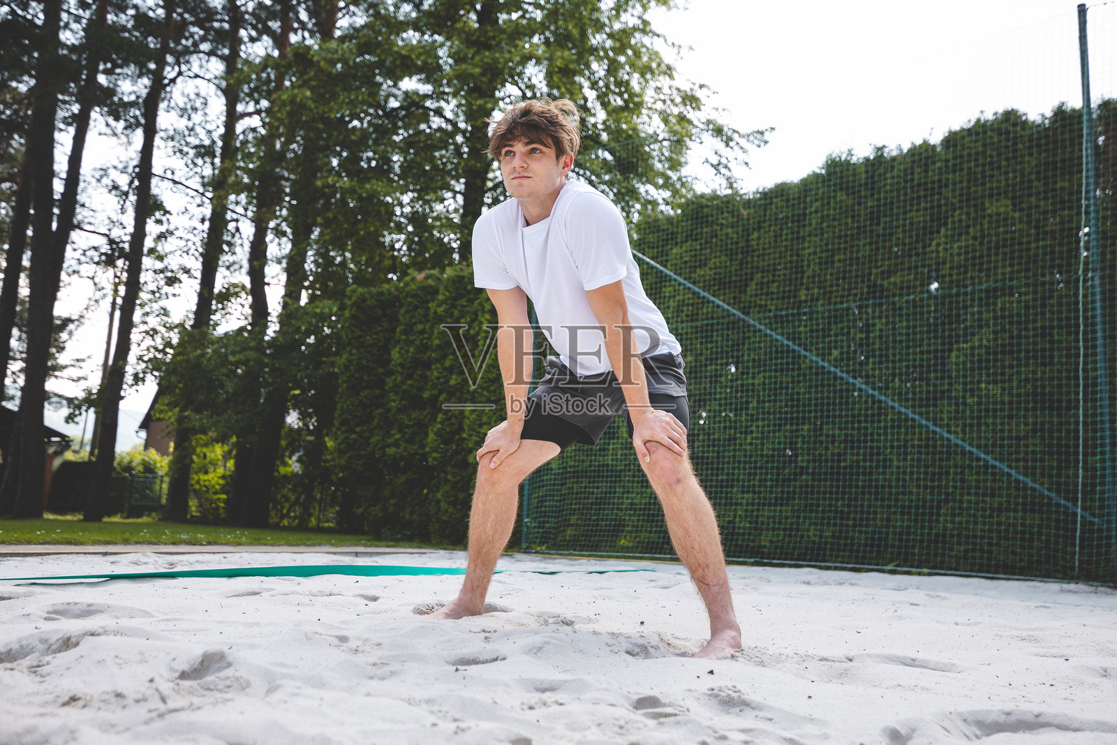 年轻男子处于准备姿势,准备在沙滩场地接球或挖球。捕捉沙滩排球在户外环境中的紧张与专注。照片摄影图片