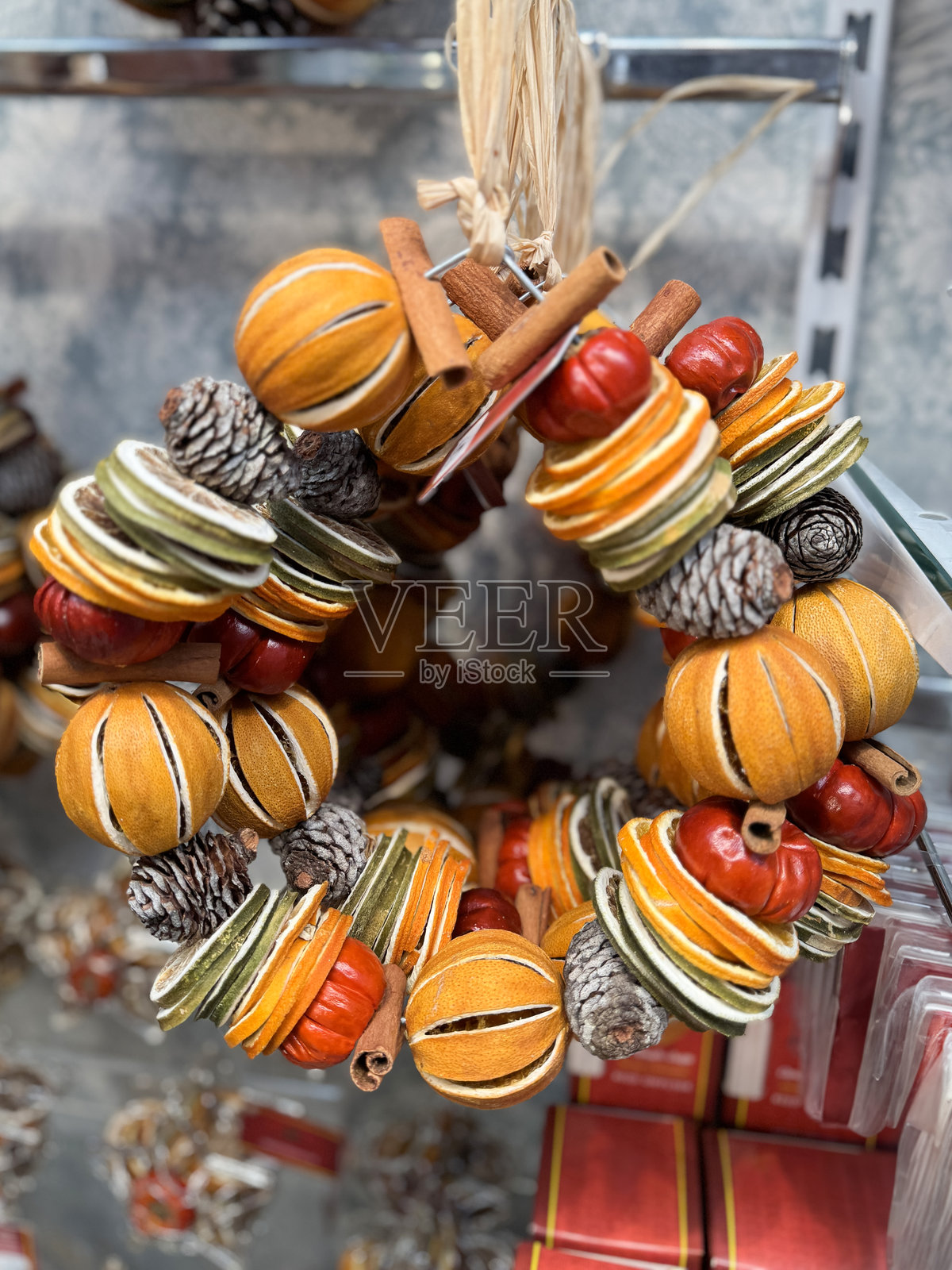 全景图展示了圣诞装饰,铁丝框架编织的花环上挂满了完整的、切片的干燥柑橘水果(橙子和青柠)、松果、小南瓜和肉桂棒,悬挂在零售展示上,前景聚焦。照片摄影图片