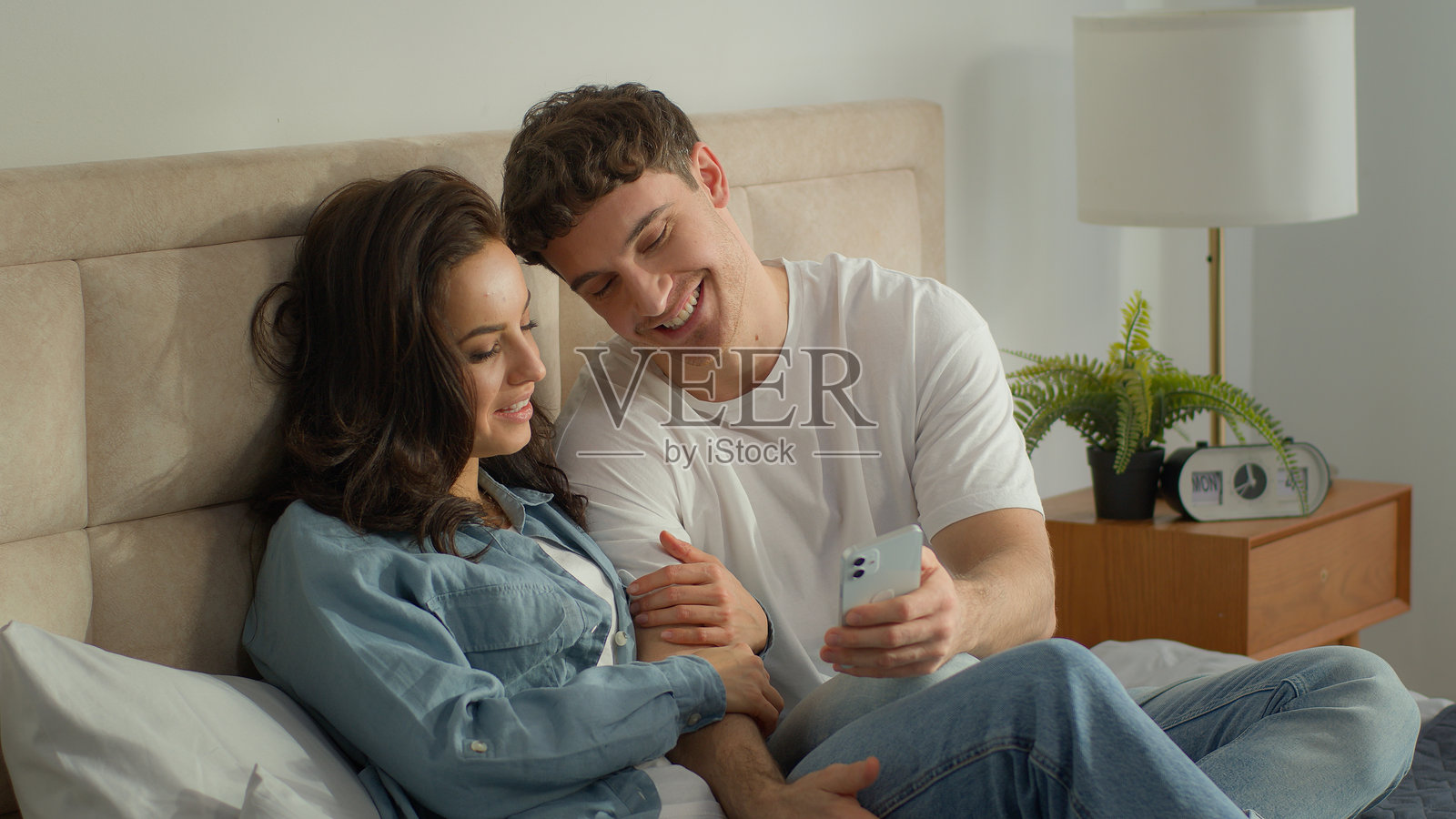 情侣在卧室里一起使用手机,男士和女士欢笑交谈,展示数字科技。照片摄影图片