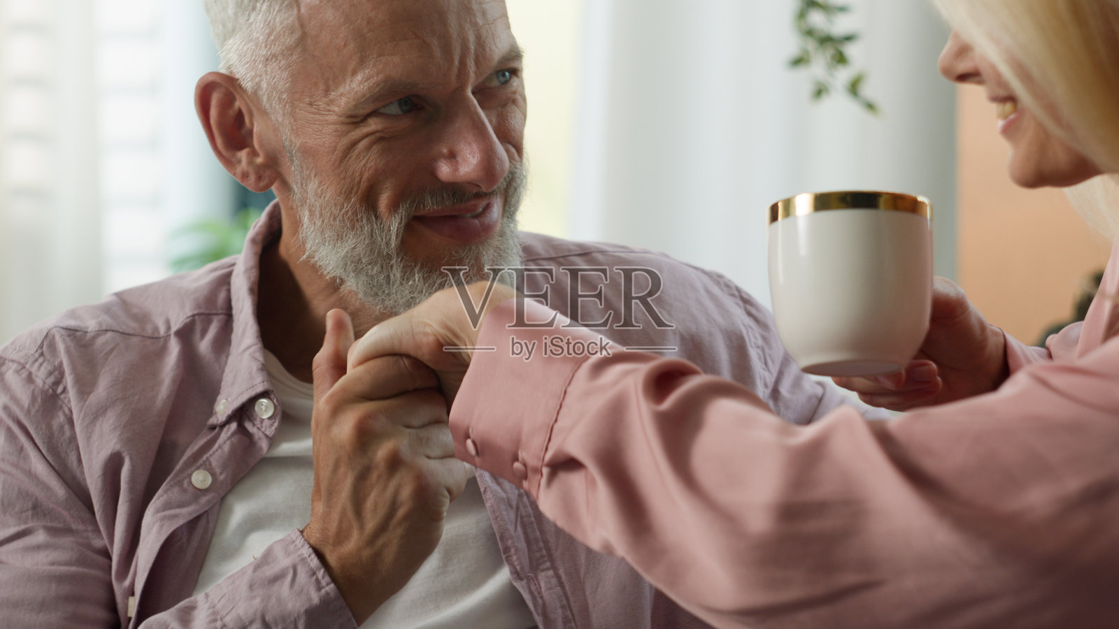 快乐的白人已婚夫妇在家中享受浪漫时光,深爱的丈夫亲吻心爱的妻子的手,妻子则在喝香浓的咖啡,二人一起度过周末,享受浪漫的时刻和亲密的情感。照片摄影图片