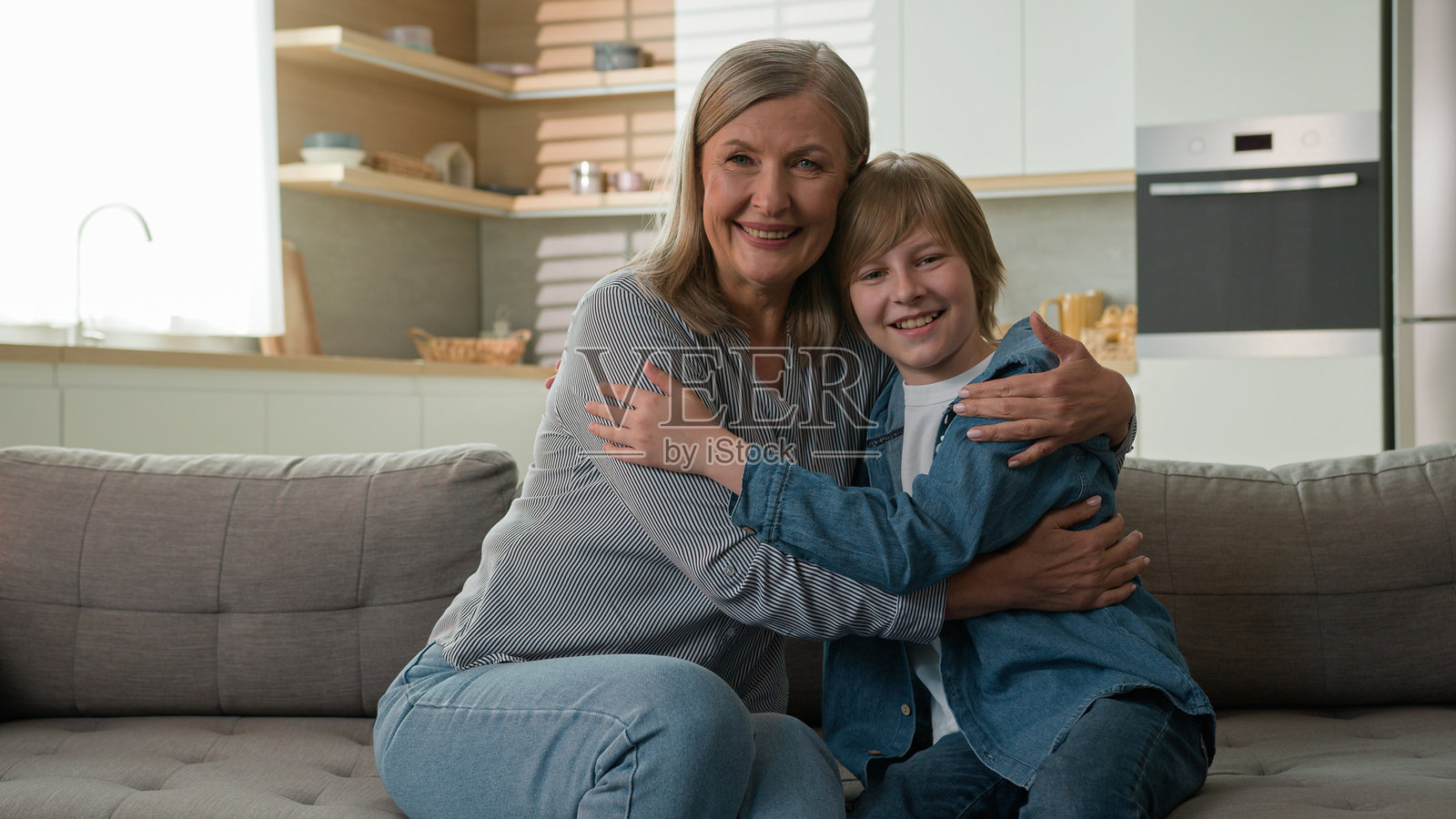 快乐的60多岁白人祖母微笑着,与孙子亲密交谈,温暖地拥抱着小男孩,坐在家中的沙发上,展现出幸福的家庭关系。照片摄影图片