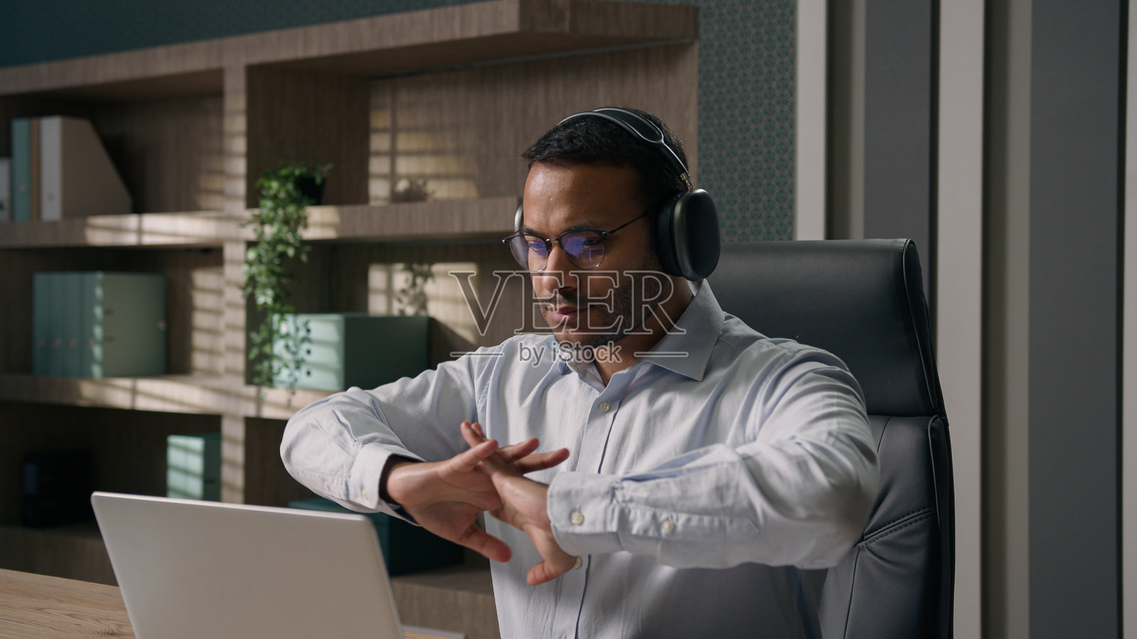 印度商人伸展手指准备开始工作,阿拉伯人和美国办公室员工在电脑前打字,听着耳机里的音乐,心情积极。照片摄影图片