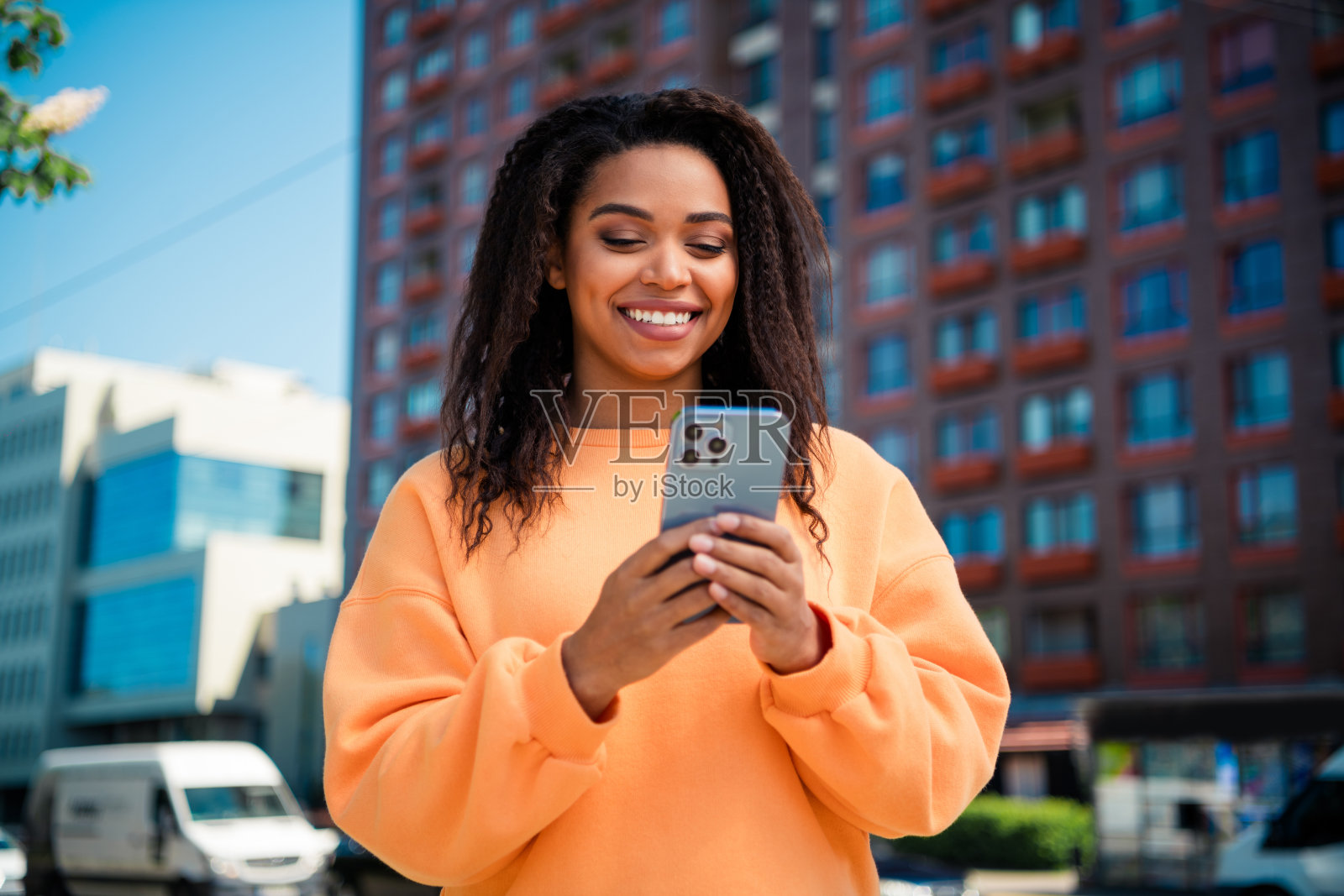 穿着橙色毛衣的漂亮快乐女士在城市街道上走着,边聊天边使用现代设备。照片摄影图片