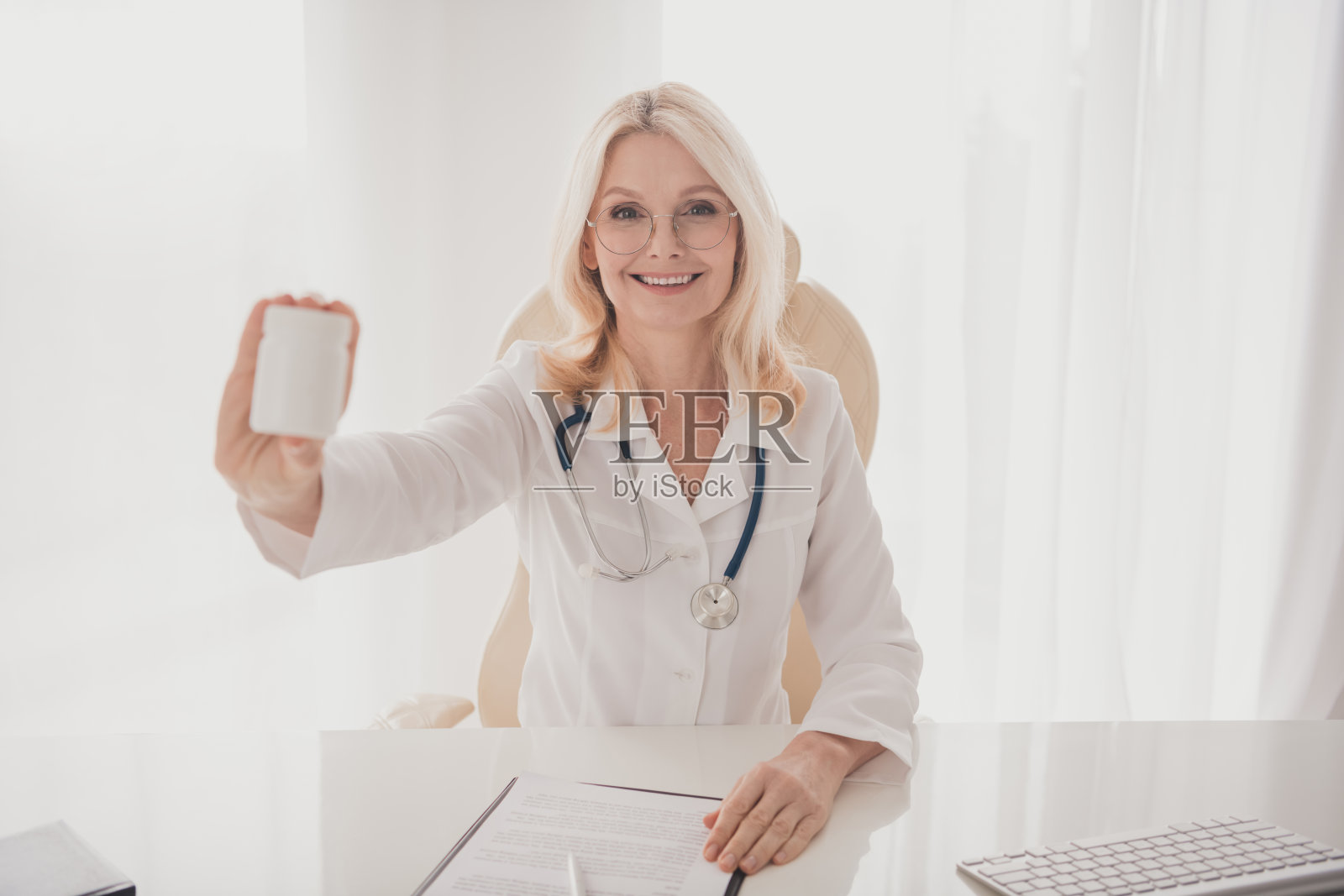 微笑的老年女医生在诊所办公室里手持药瓶,准备为患者提供医疗咨询和健康建议照片摄影图片