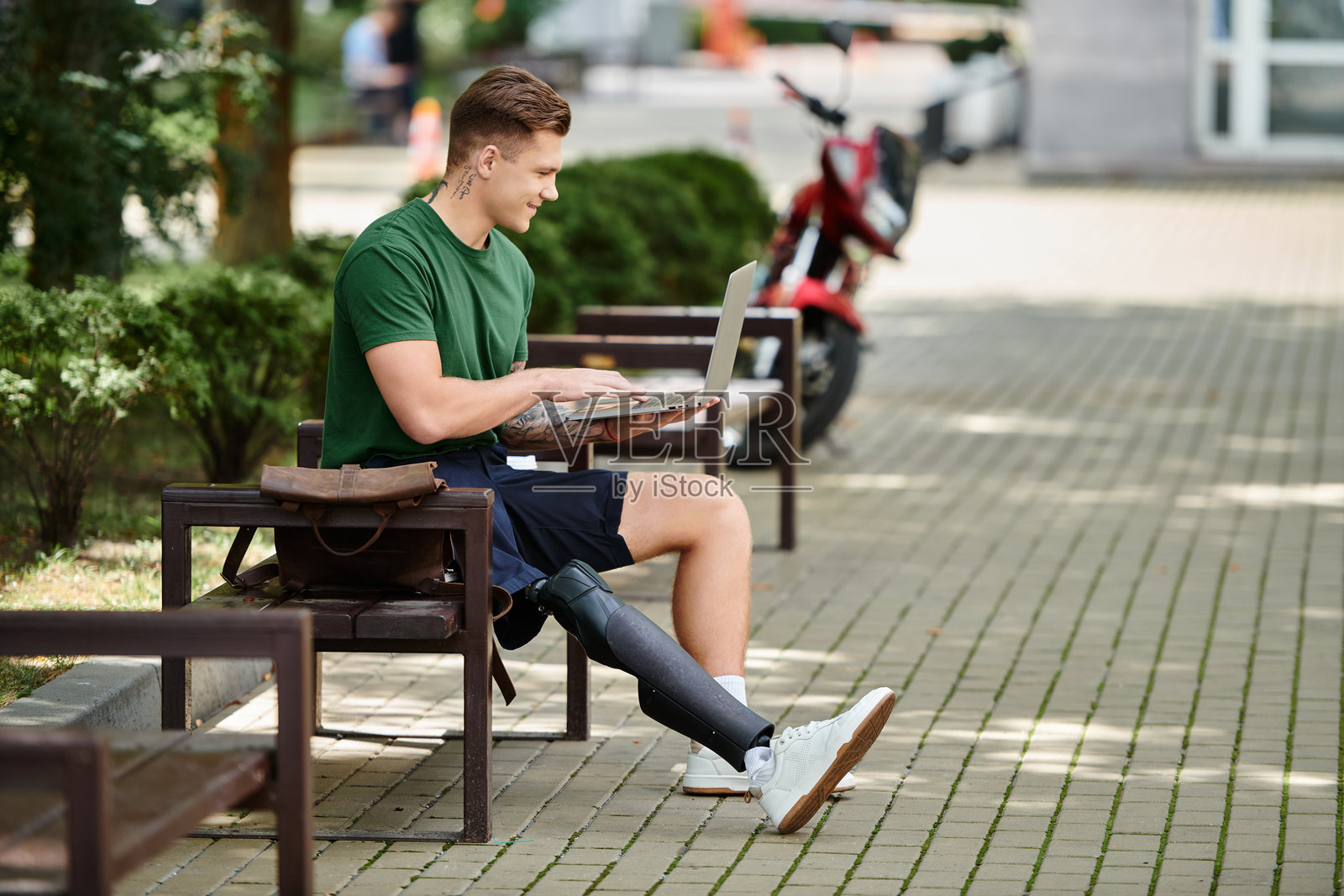 年轻男子在宁静的户外环境中使用笔记本电脑,配有义肢。照片摄影图片
