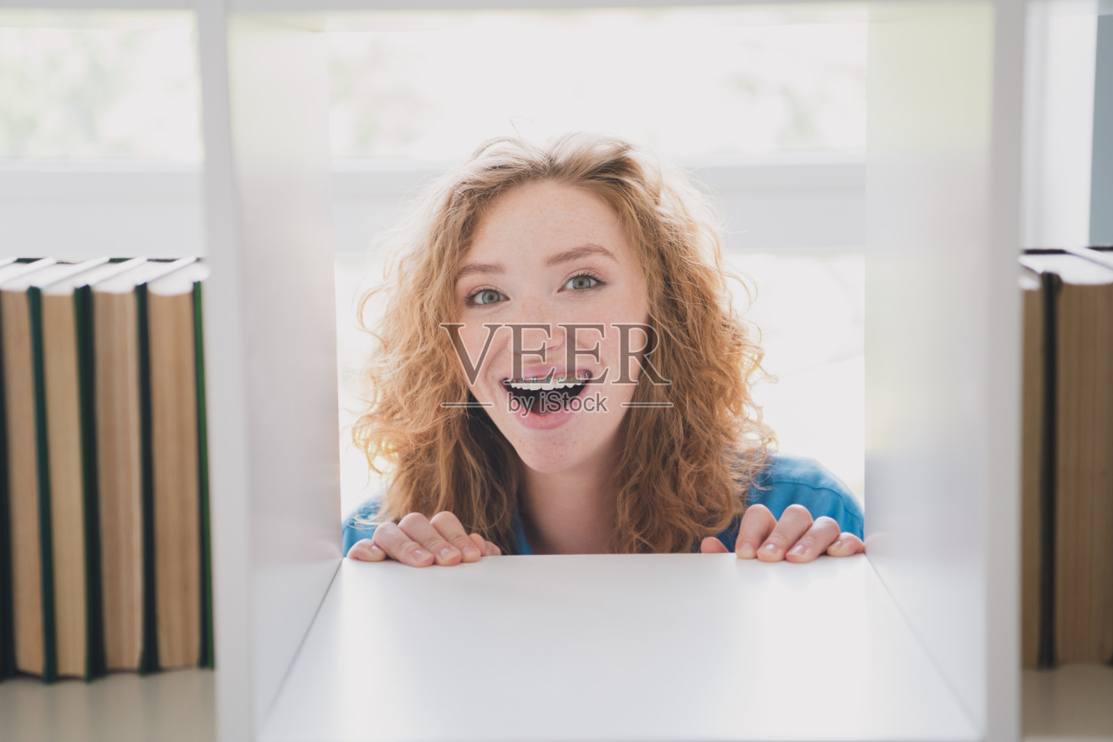 一位可爱的姜色头发年轻女孩,兴奋地微笑着,穿着蓝色衣服,在现代舒适的室内公寓中阅读书籍。照片摄影图片