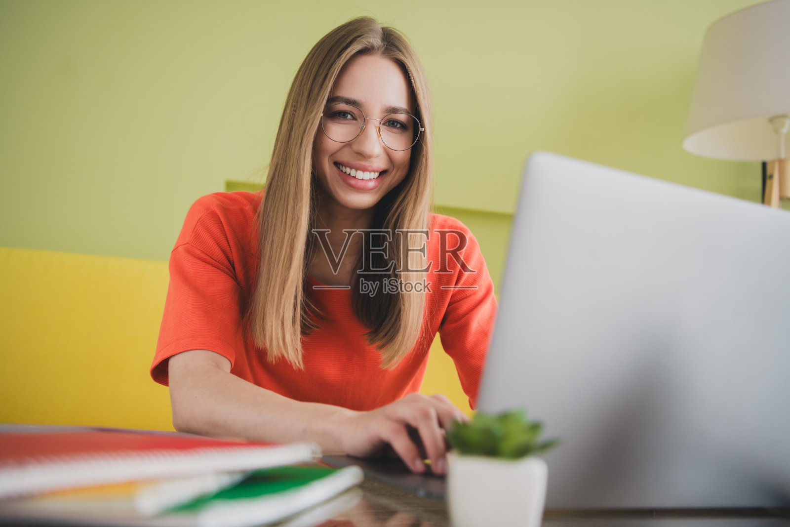 可爱的年轻女孩穿着橙色衣服在宽敞的房子里使用笔记本电脑,春天的室内环境。照片摄影图片