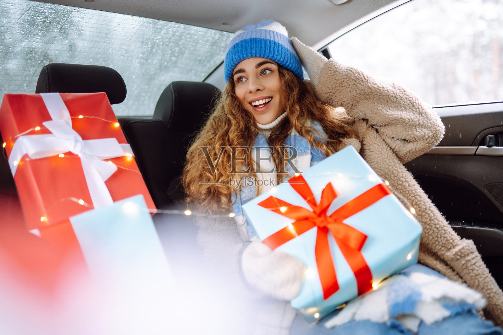 年轻女性坐在车后座,旁边是精美包装的圣诞礼物。照片摄影图片