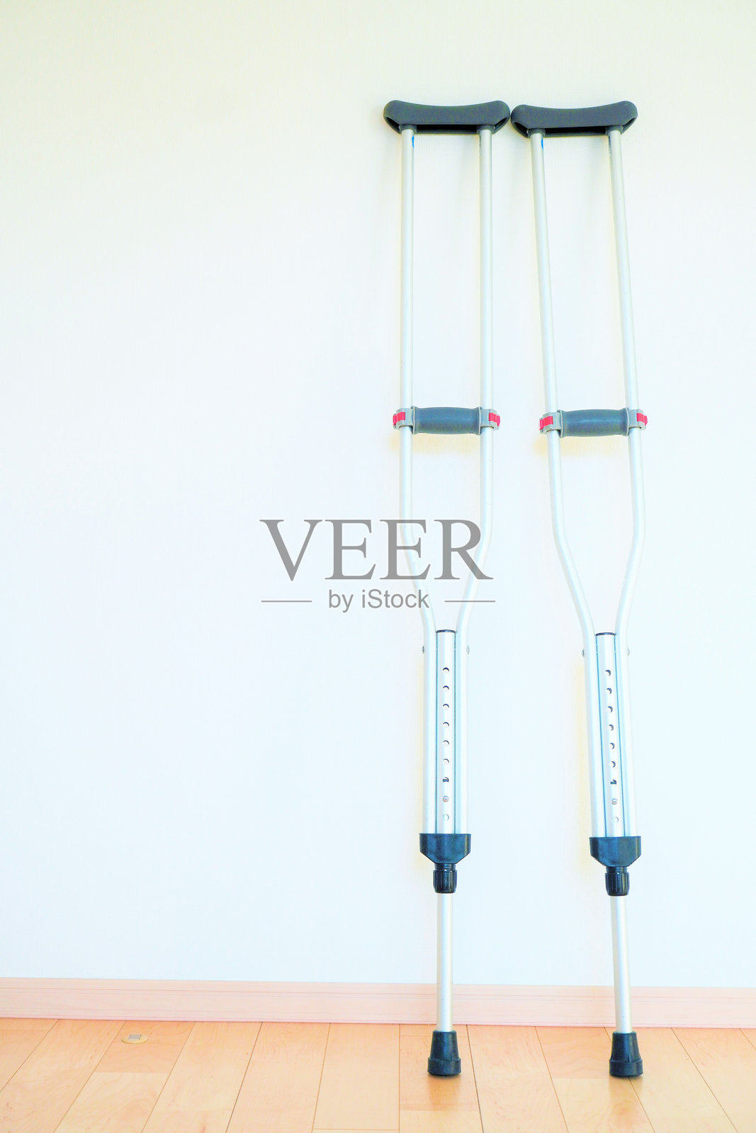 拐杖靠在室内木地板上的白色墙壁旁。照片摄影图片