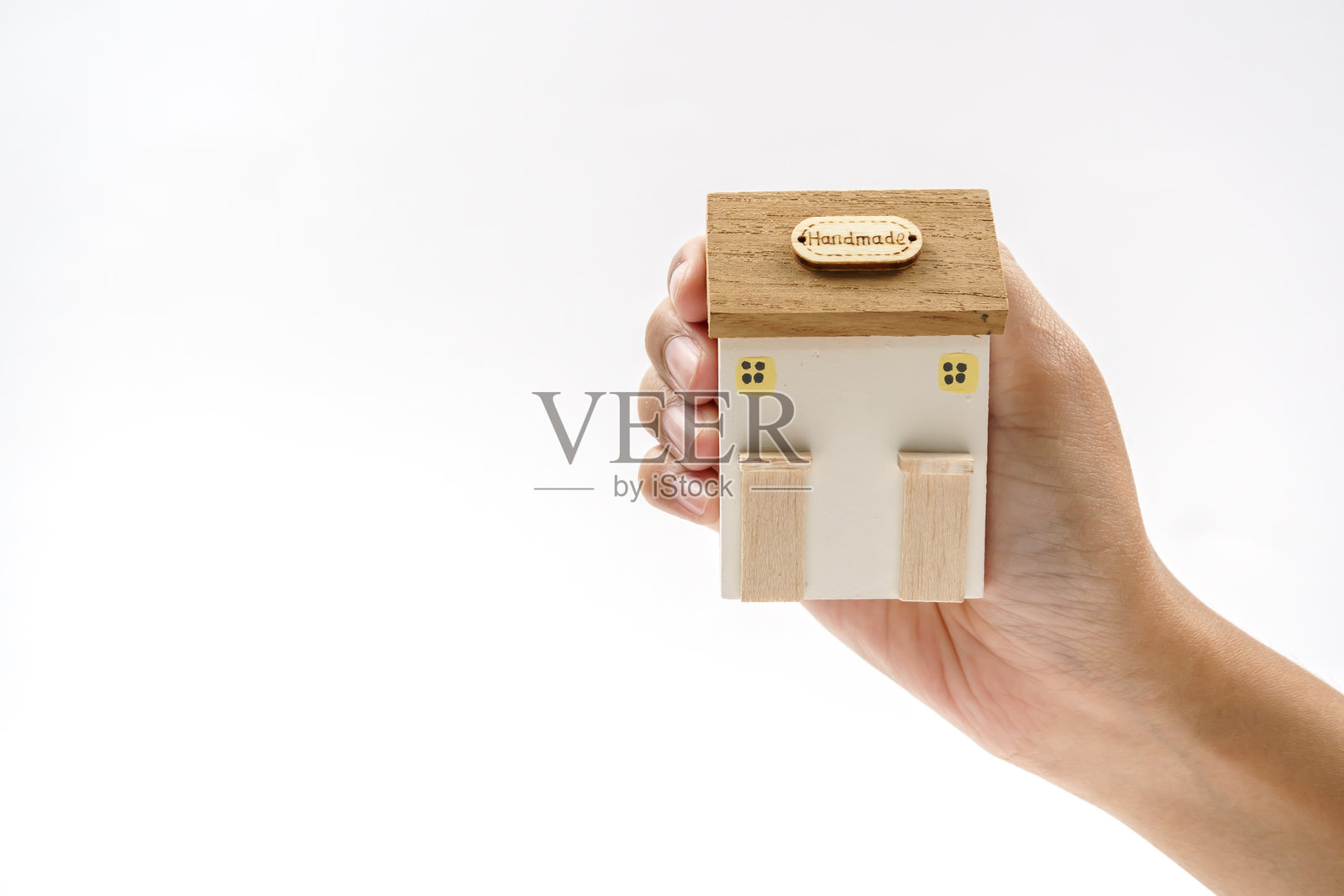 一个人手持一个小木屋模型,象征着家、温暖和舒适,置身于简约的环境中。照片摄影图片