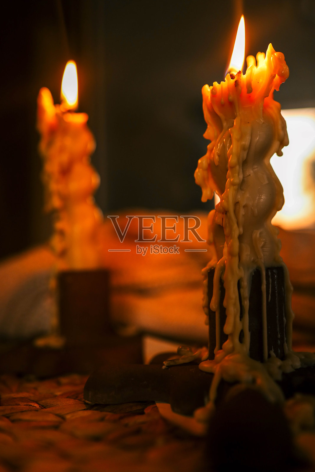 两支点燃的蜡烛特写,蜡油融化,营造出温馨的氛围,背景是柔和灯光的房间在日落时分模糊的景象,捕捉到宁静夜晚的温暖与安详。照片摄影图片