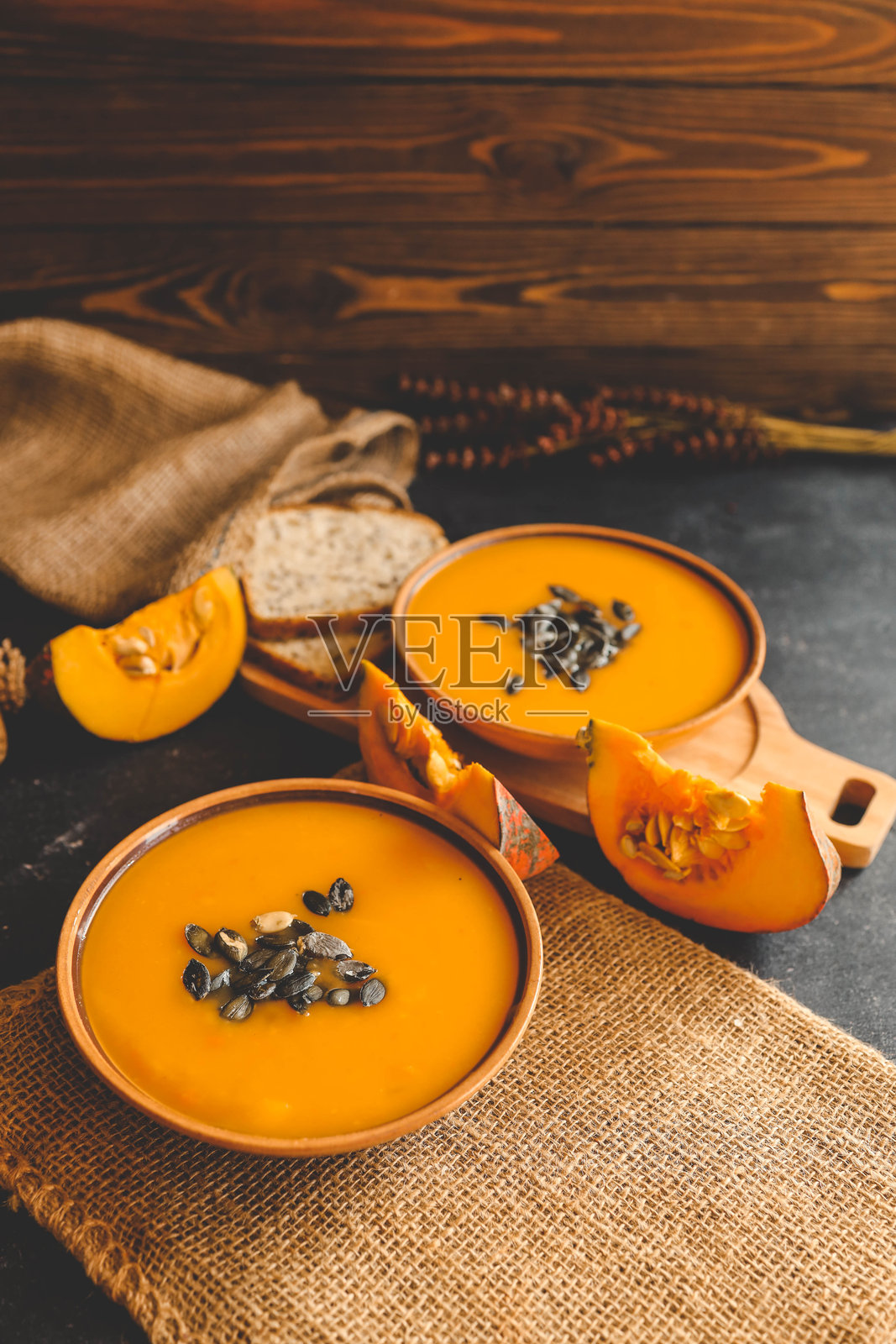 两碗南瓜泥汤,配有肉丸、南瓜籽和一枝迷迭香,横放在深色背景上。照片摄影图片