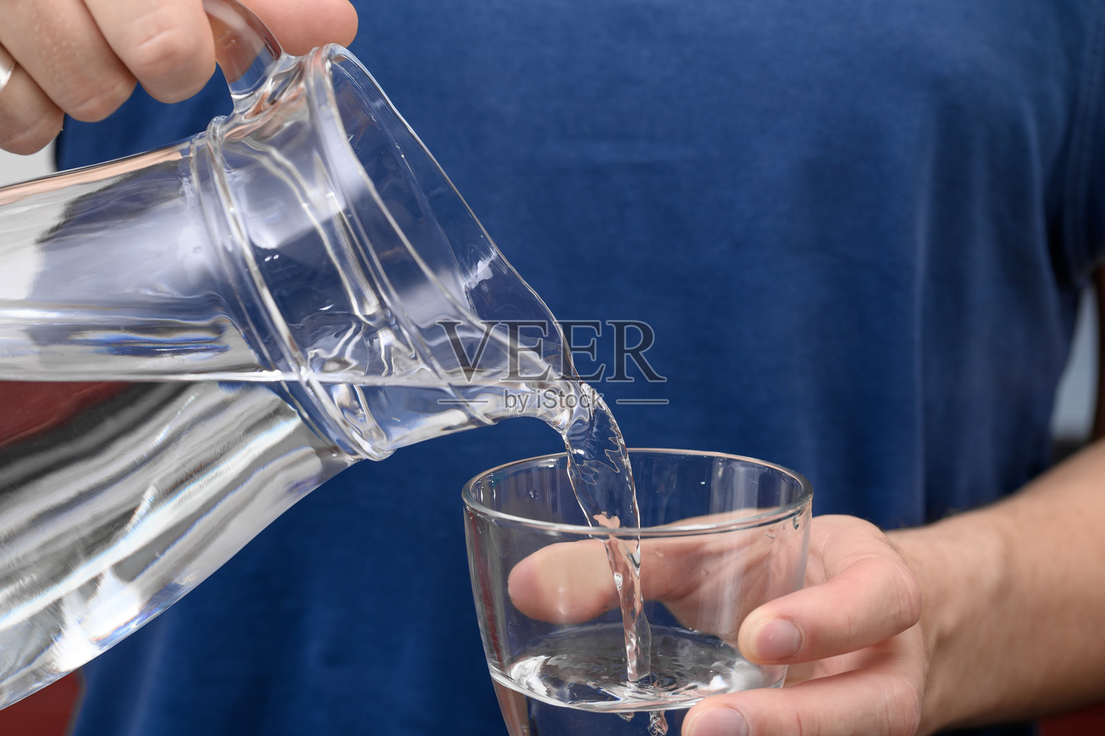 男孩从玻璃壶中倒出清澈的新鲜水到玻璃杯里照片摄影图片