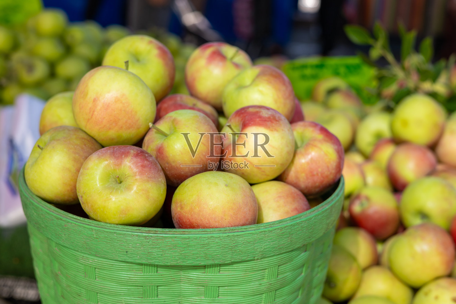 阳光明媚的下午,户外市场上堆放着新鲜的绿色和红色苹果照片摄影图片