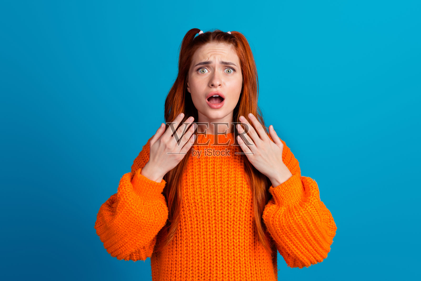 吸引人的年轻女性的照片肖像,穿着时尚的橙色针织服装,惊恐地尖叫,背景为蓝色。照片摄影图片