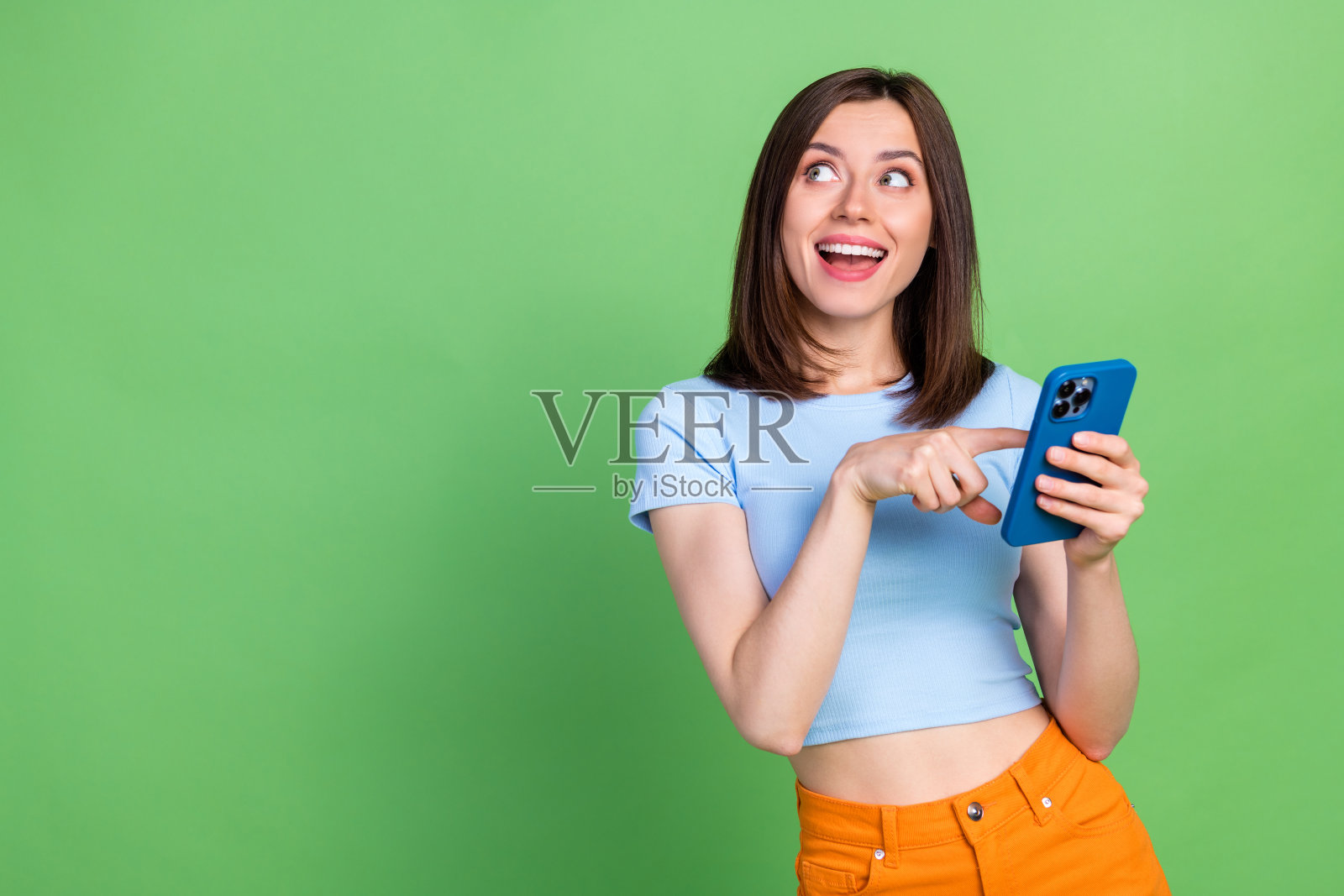 兴奋的快乐人用手指触碰电话,目光投向空旷的空间,背景为绿色。照片摄影图片