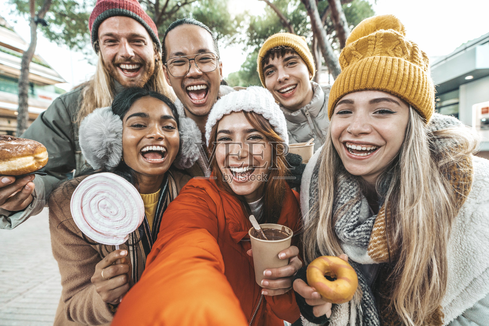 快乐的朋友们穿着冬季衣物在户外用智能手机自拍 - 一群年轻人一起参观圣诞市场,享受冬季假期。照片摄影图片