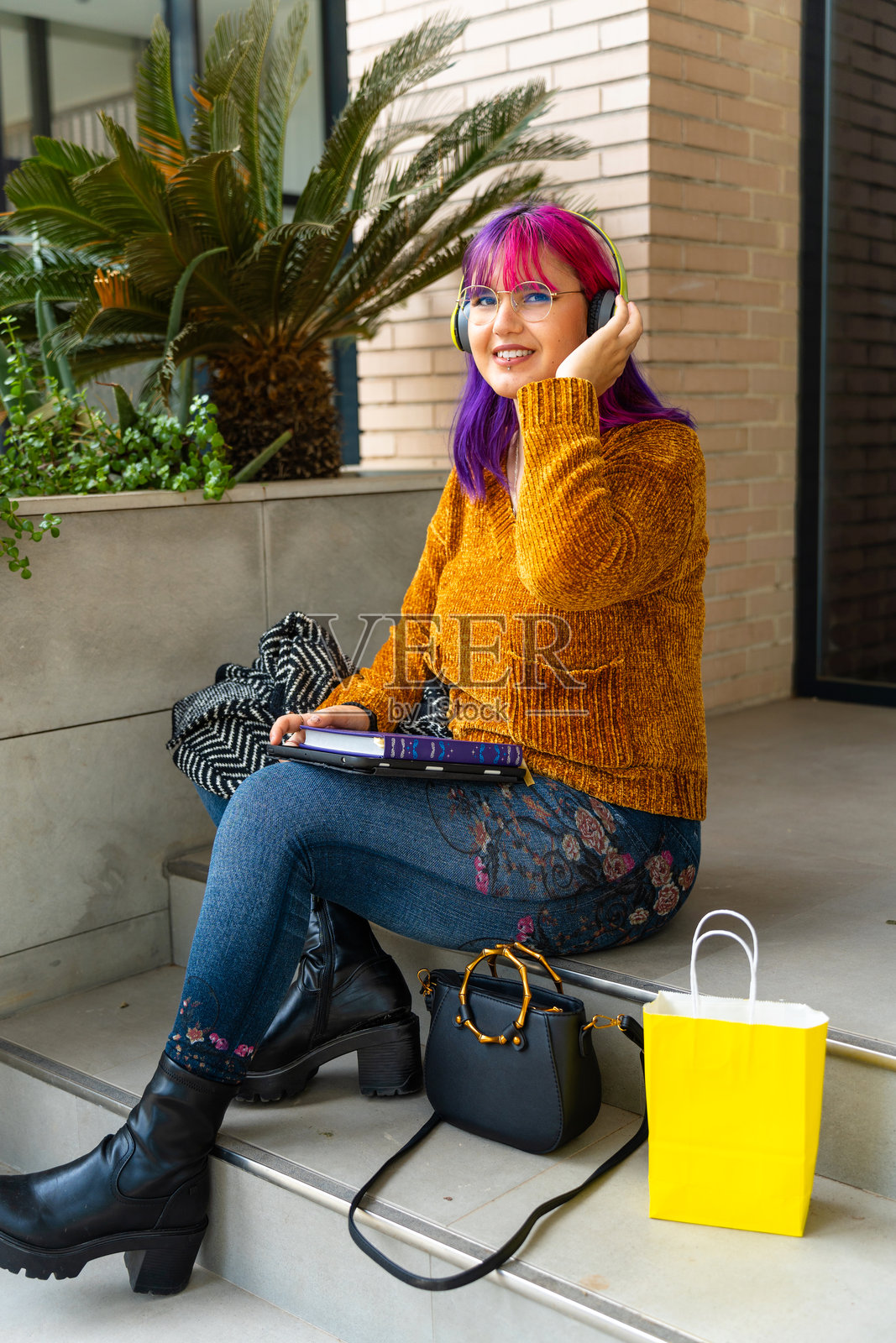 身材积极的自闭症女孩坐在她家门口的台阶上,留着粉色头发。照片摄影图片