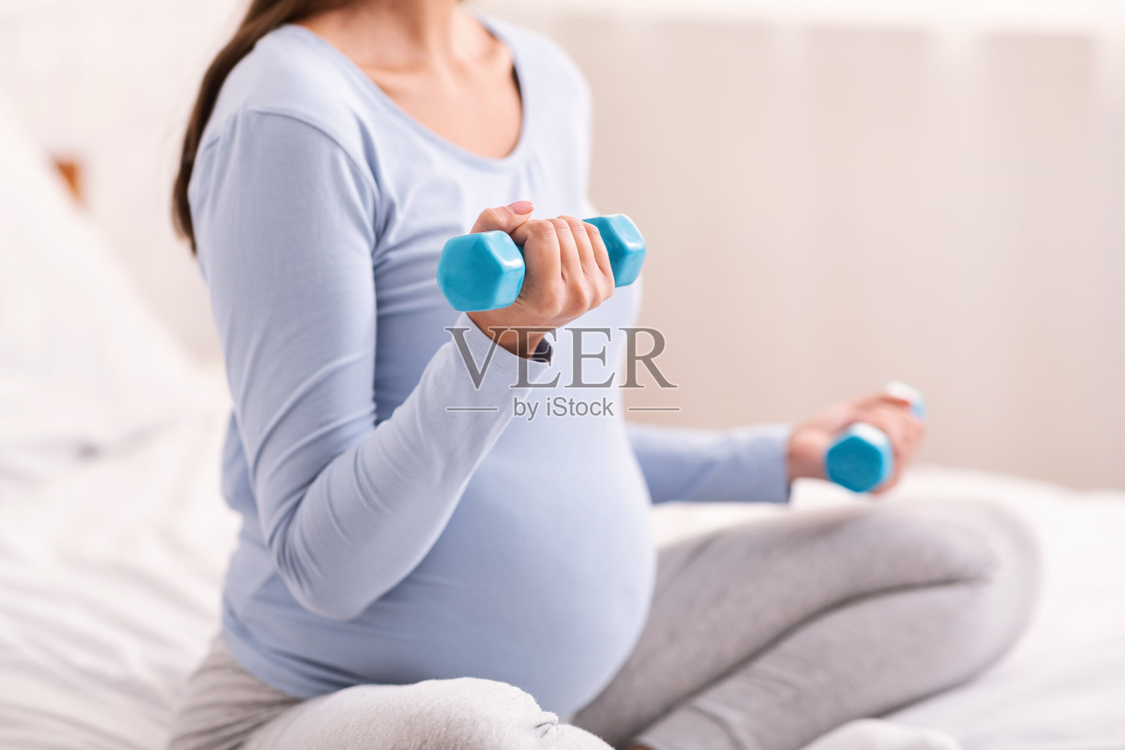 无法辨认的孕妇在室内床上坐着用哑铃锻炼照片摄影图片