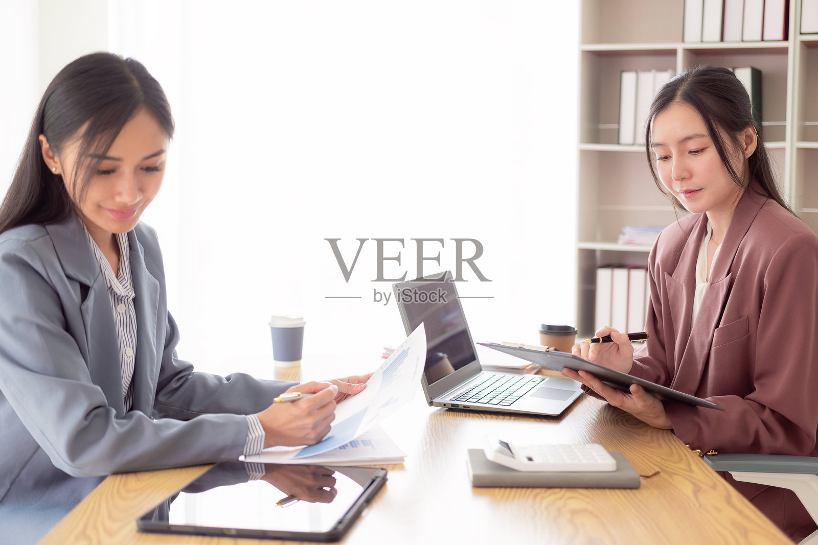 两位亚洲女性正在讨论如何通过使用计算器处理财务图表文件来改变她们的商业想法,以增加利润和增强业务实力。照片摄影图片