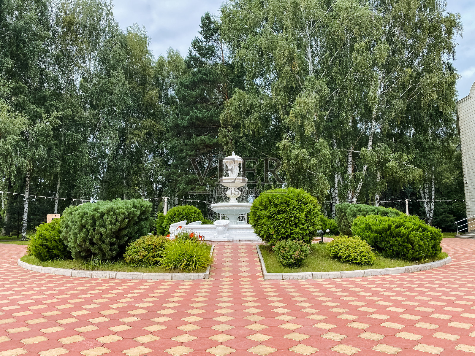 公园中央有一个美丽的喷泉,优雅地被各种郁郁葱葱的树木和生机勃勃的灌木环绕,为游客创造了一个宁静的氛围。照片摄影图片