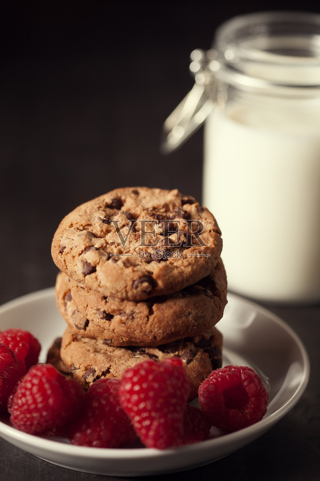 带有红覆盆子的巧克力曲奇饼干和牛奶,背景为乡村风格的木材。照片摄影图片