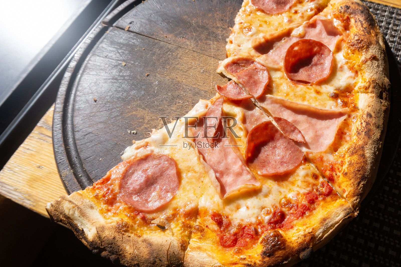 海边的餐厅和比萨店。阳光下,木板上放着意大利香肠、辣香肠和火腿的比萨饼俯视图。照片摄影图片