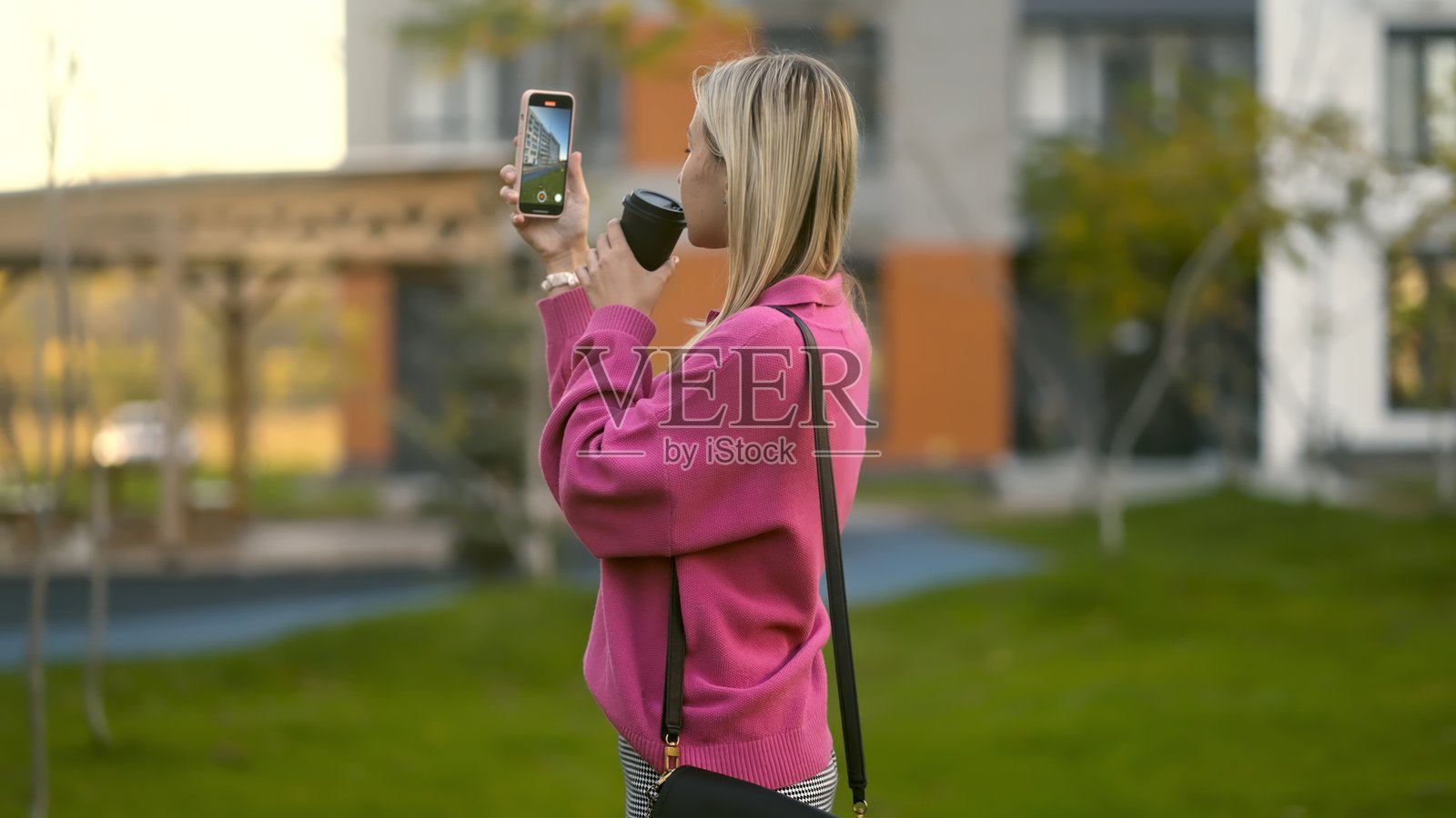 一位穿着粉色毛衣的女性在户外拍照,享受捕捉回忆的乐趣。照片摄影图片