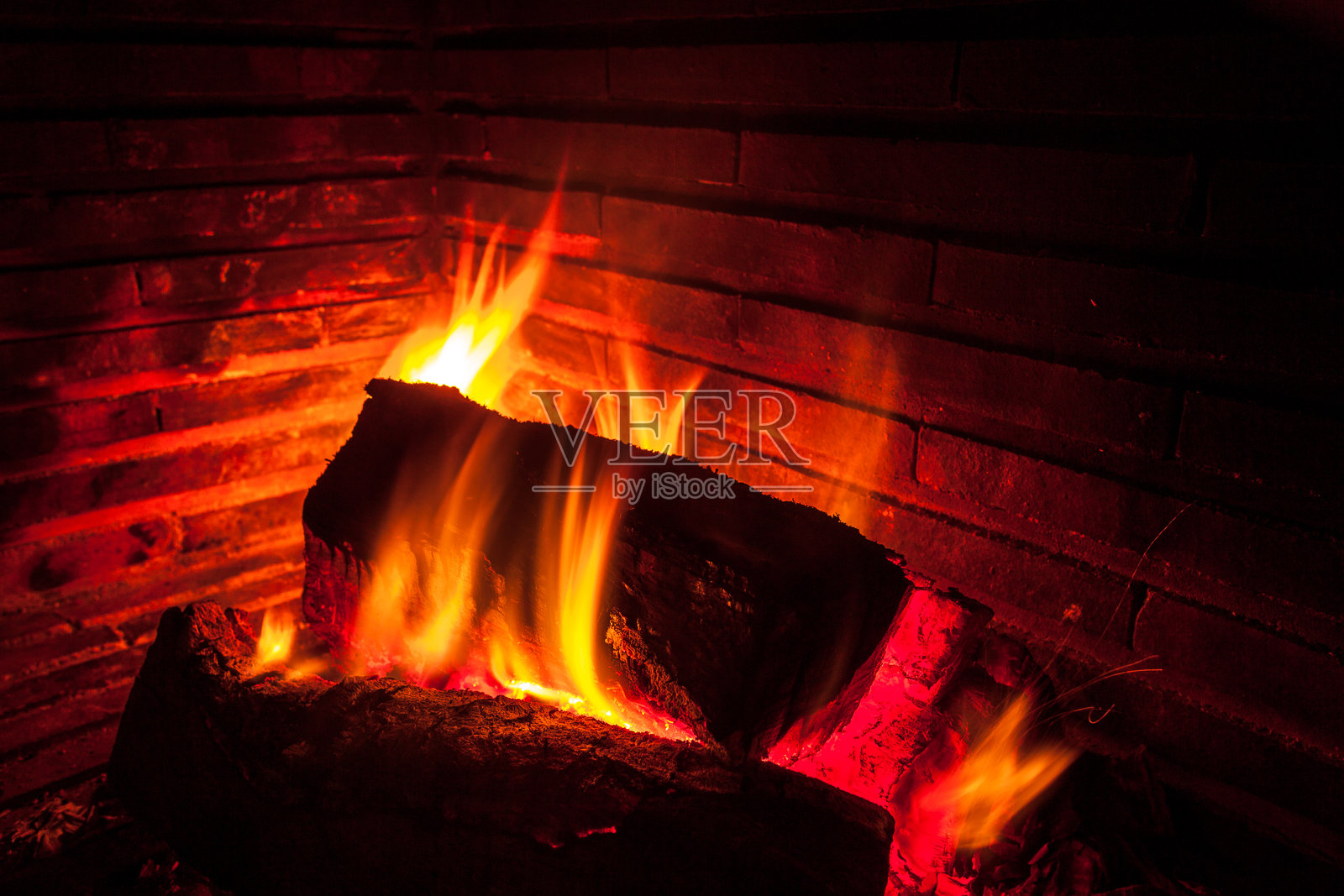 壁炉中燃烧的火焰特写。火焰在木柴周围跳动,散发出强烈的橙色光芒和深红色的余烬,营造出温暖舒适的氛围。照片摄影图片