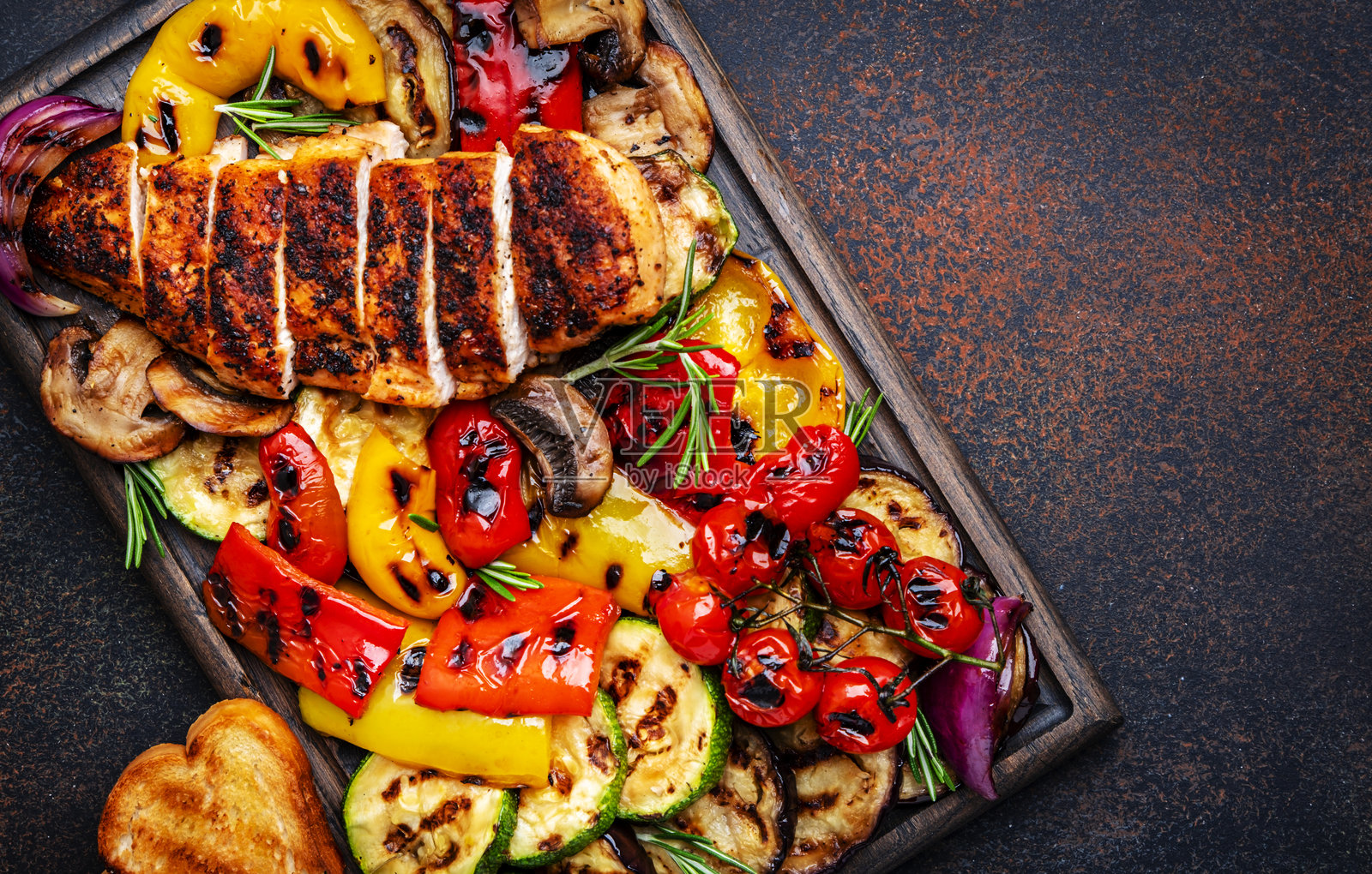 烤吧!橡木托盘上的烤鸡、蔬菜、蘑菇和吐司。棕色背景,俯视图。照片摄影图片