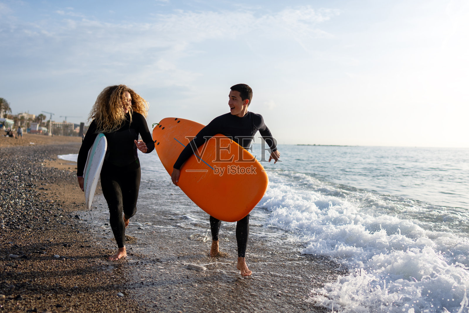 美丽快乐的冲浪情侣在海滩上玩耍,手持冲浪板奔向海浪照片摄影图片