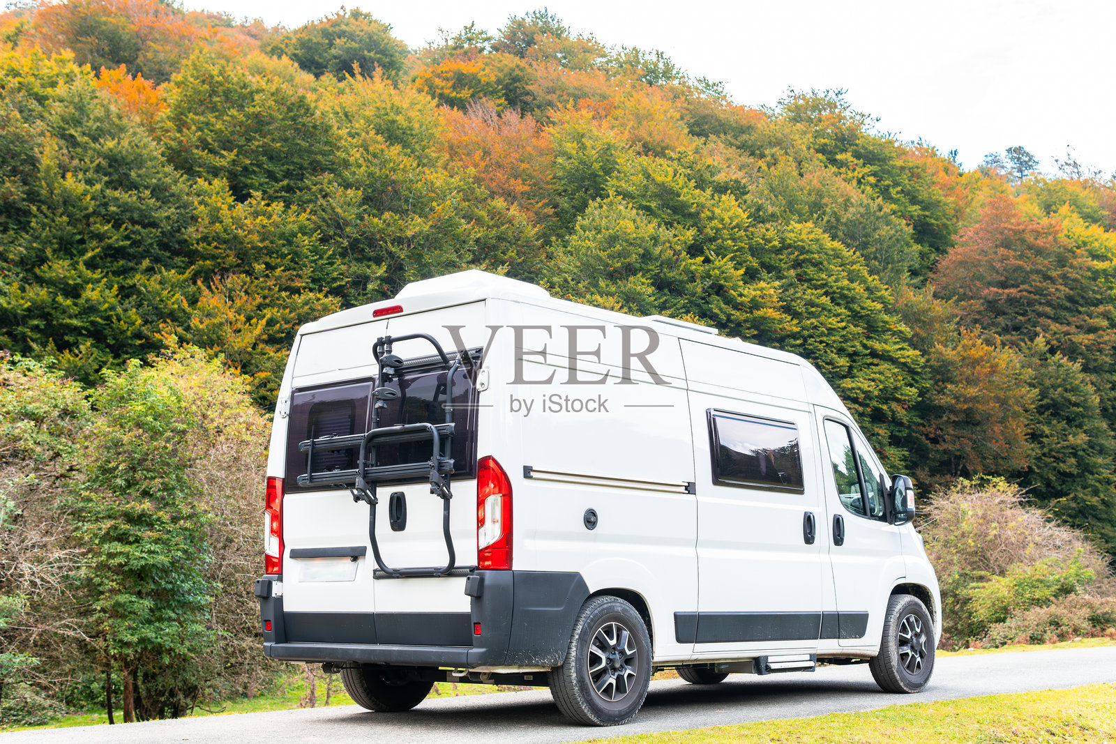 一辆房车沿着山路穿过五彩斑斓的秋季森林。概念:自由旅游,房车旅行,房车在自然和山脉中。照片摄影图片