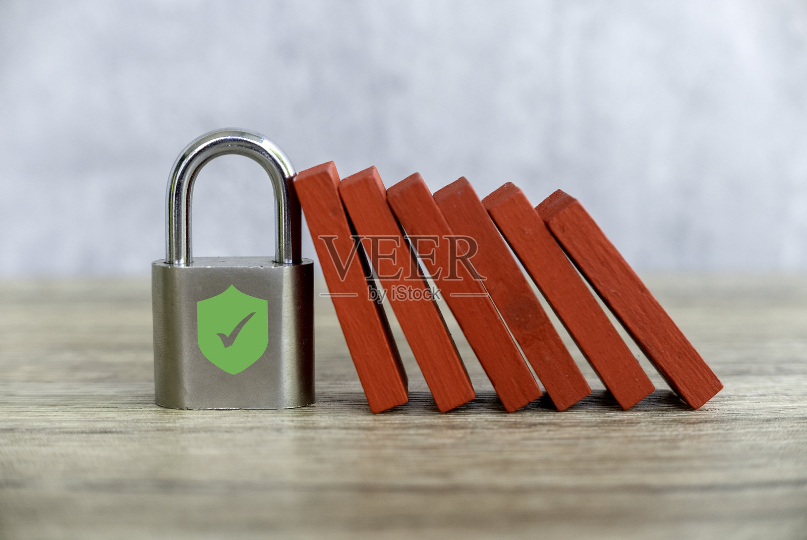 带有安全盾的挂锁阻挡着掉落的红色多米诺骨牌,放置在木质表面上照片摄影图片