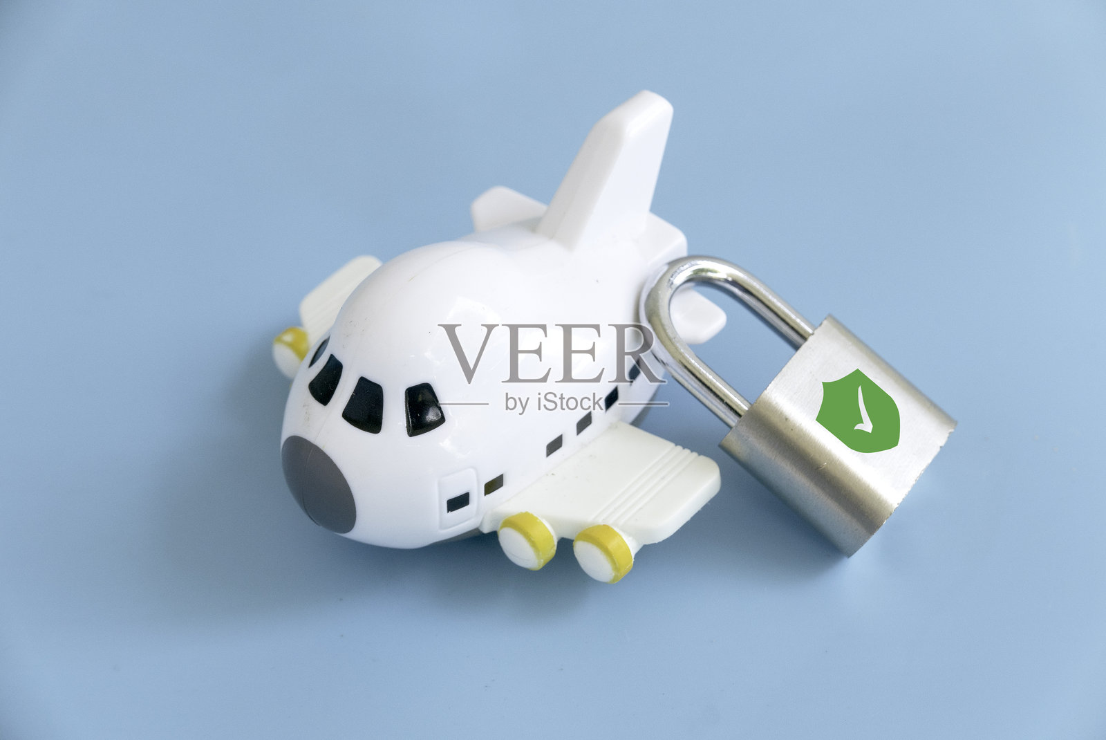 安全冒险:一个带有盾牌和勾号的挂锁旁边放着一架玩具飞机照片摄影图片